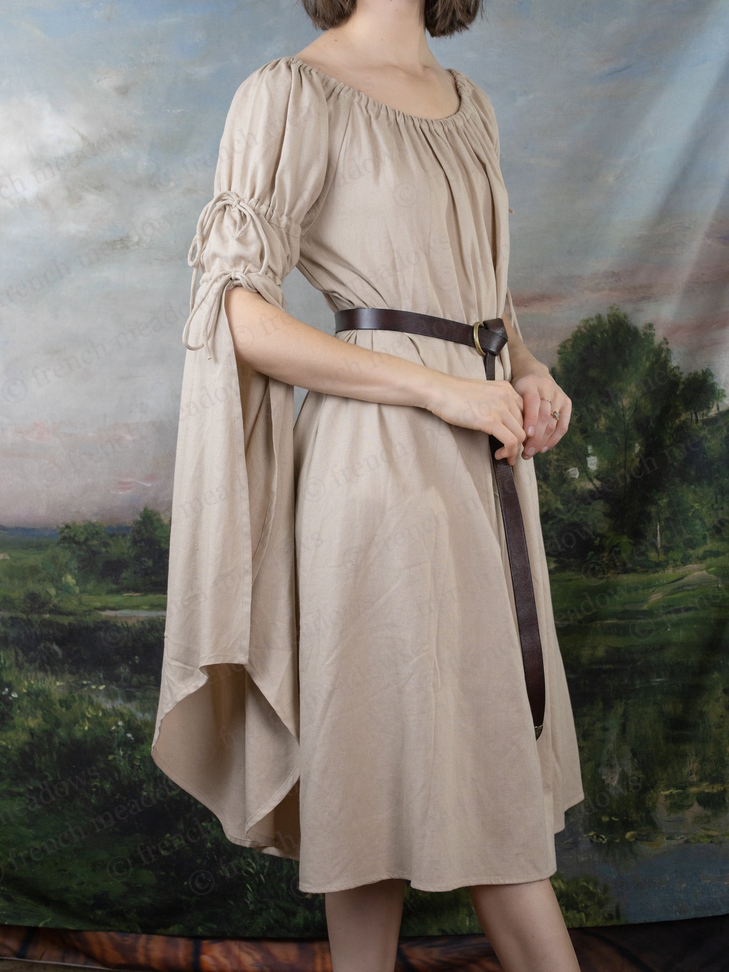 Natural Linen Bell Sleeve Chemise shown with elastic neckline, flowing sleeves, and brown belt against pastoral backdrop