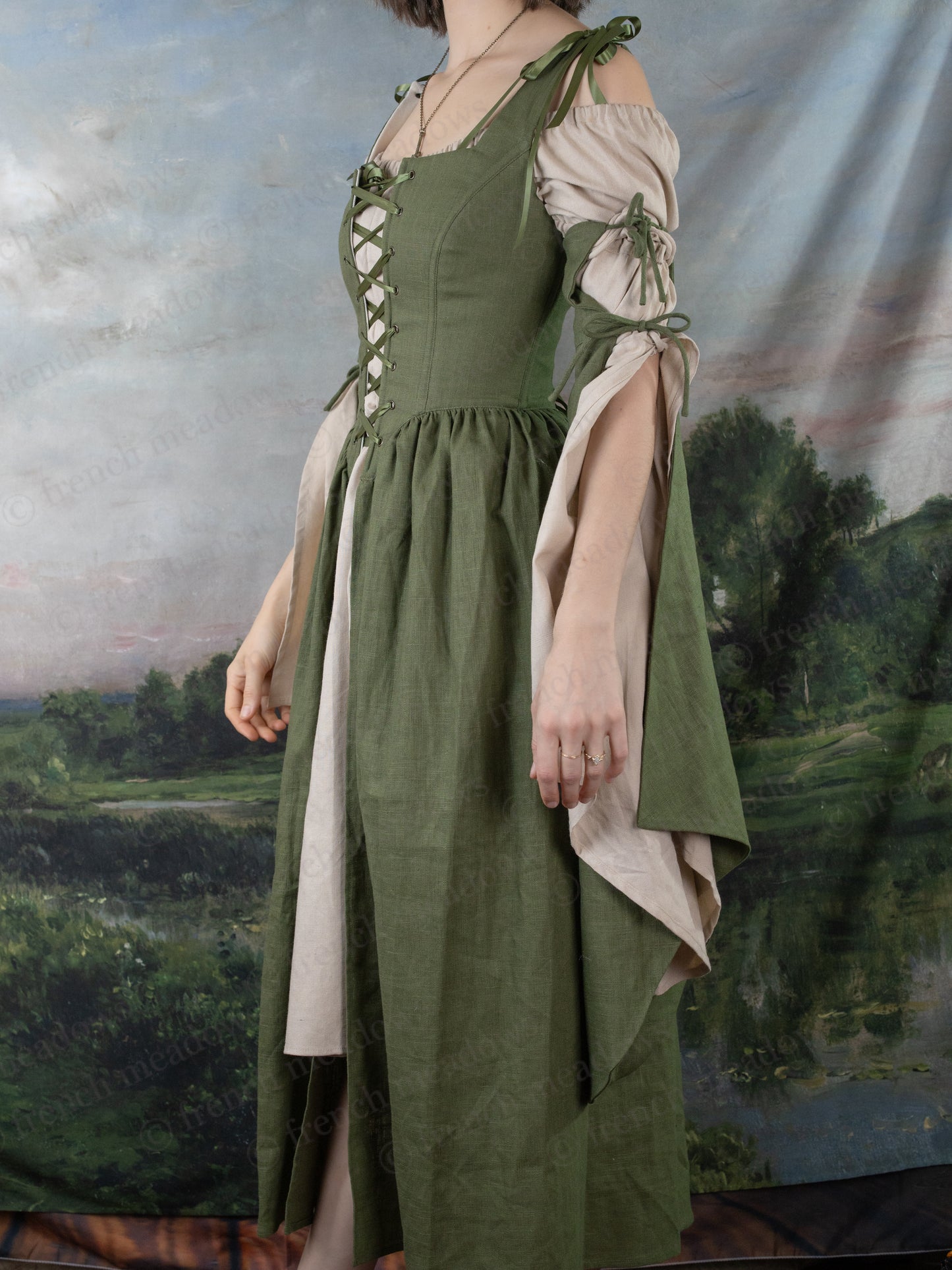 Natural Linen Bell Sleeve Chemise shown with green medieval-style dress, featuring off-shoulder design and flowing sleeves against pastoral backdrop