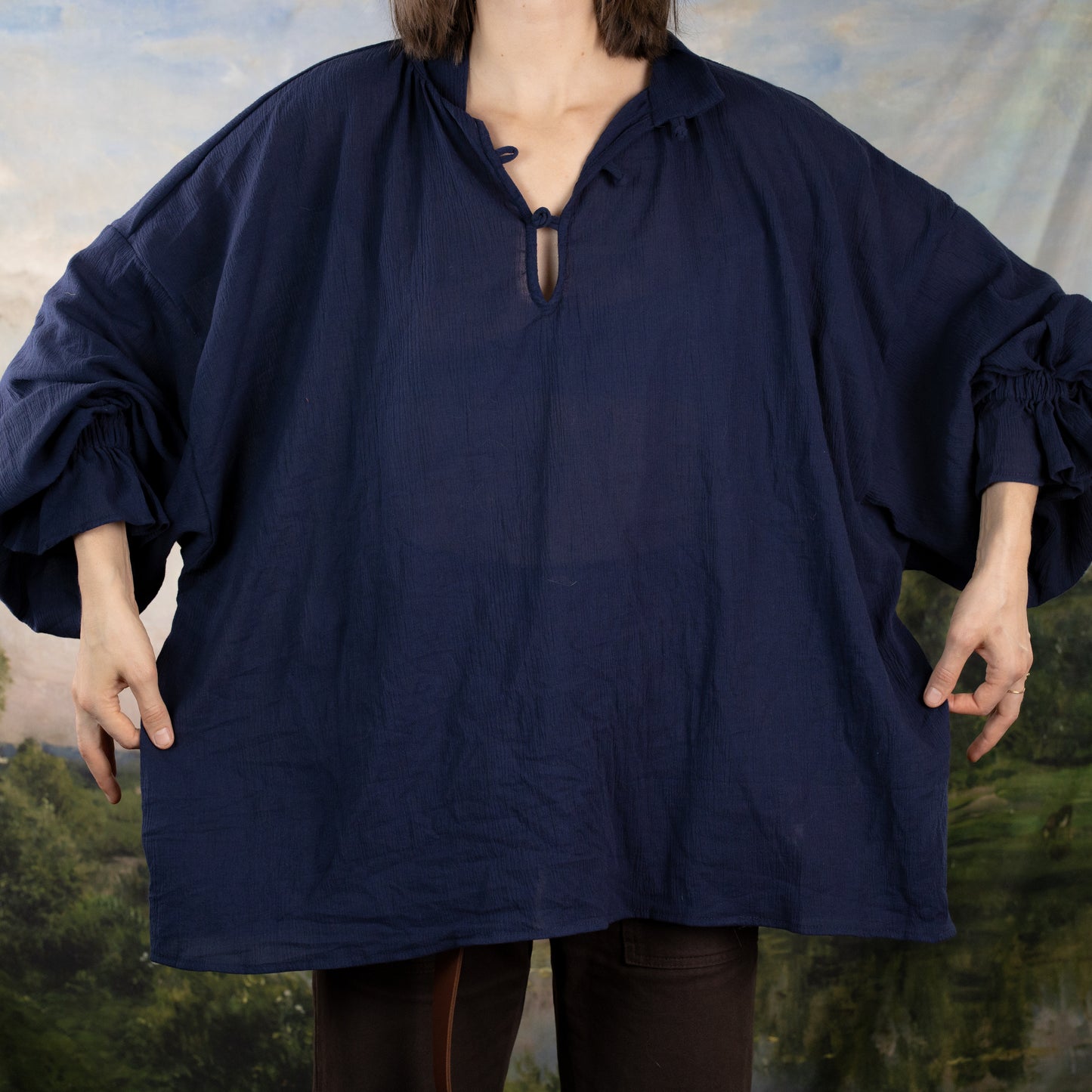 Darcy Shirt in navy blue cotton with billowing sleeves and knotted neckline shown against pastoral backdrop