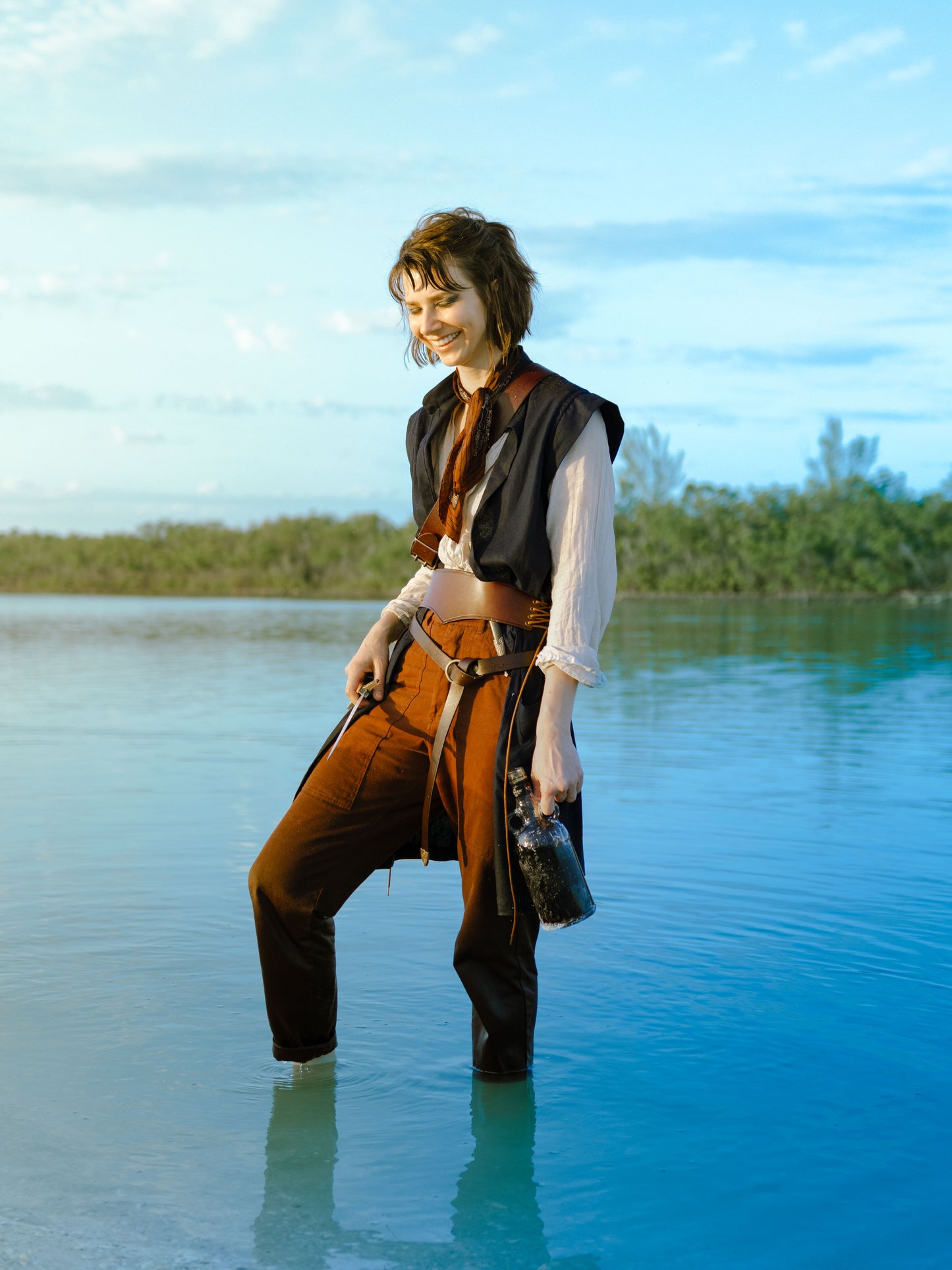 Navy Pirate Vest shown in outdoor beach setting, styled with white shirt and brown pants against turquoise water backdrop