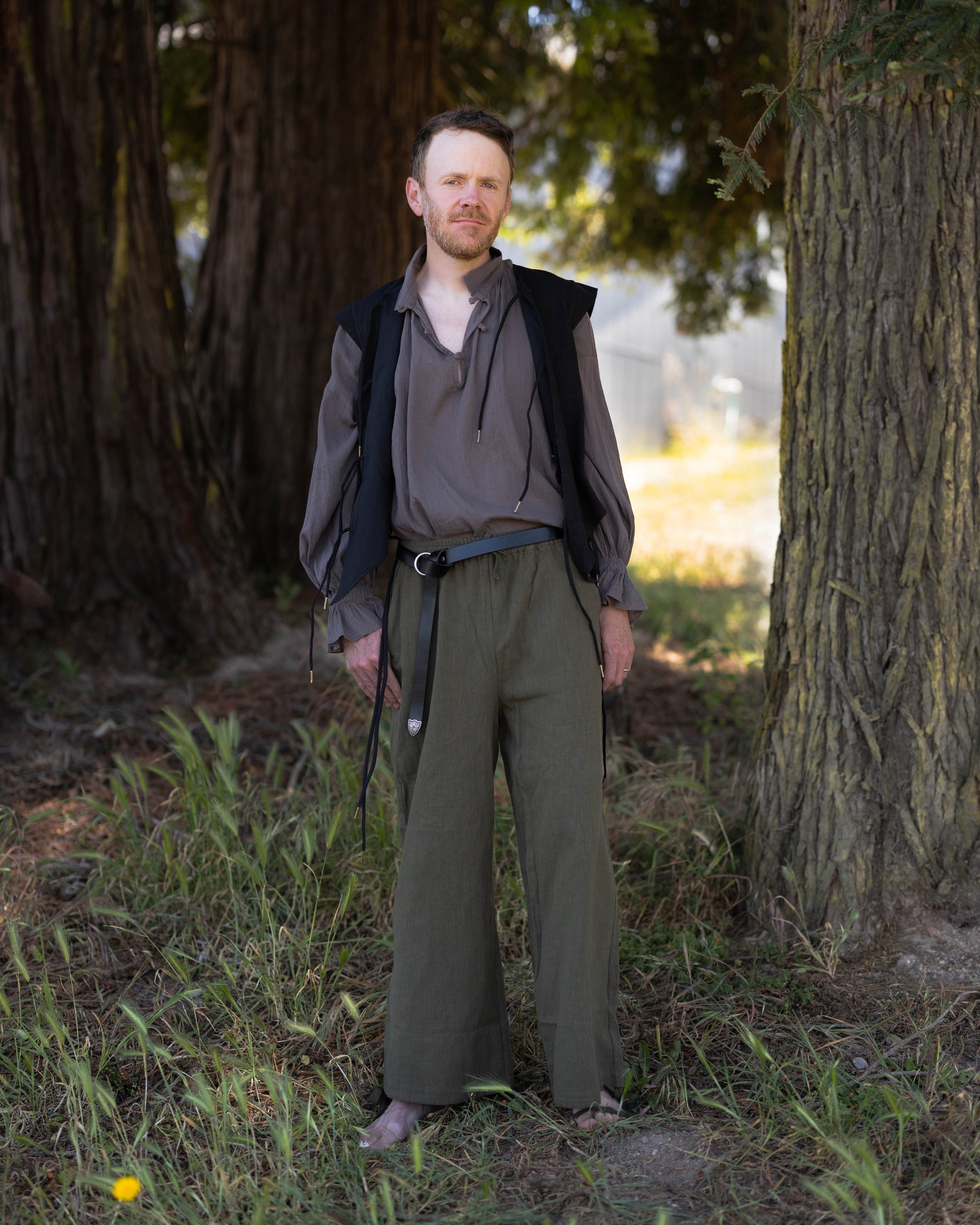 Man wearing a Black Bard Vest with a loose shirt and wide pants standing in a wooded outdoor setting.