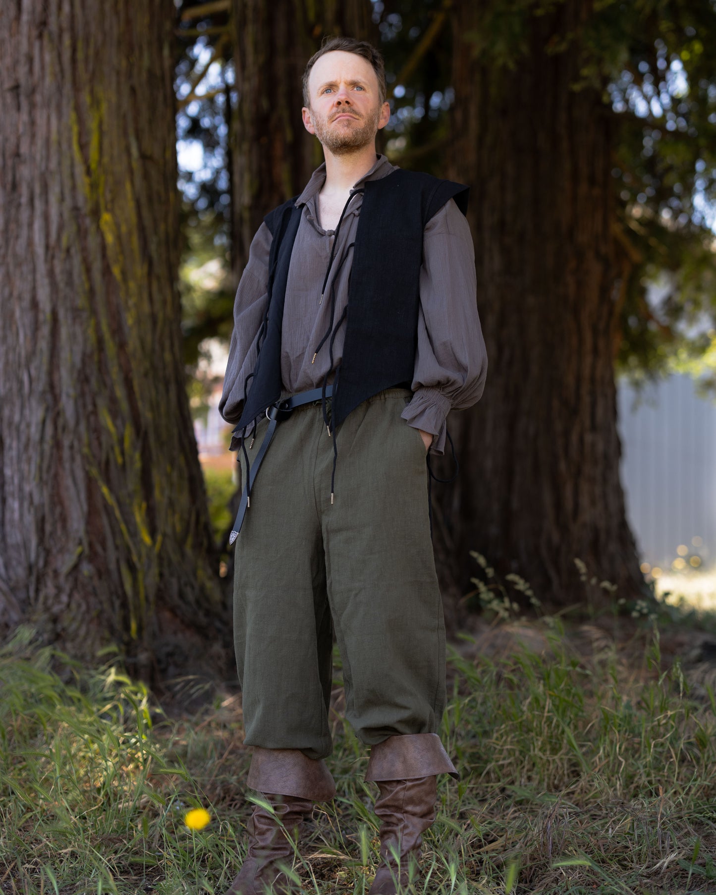 Man wearing Darcy Shirt with billowing sleeves and knotted buttons standing in forest setting.
