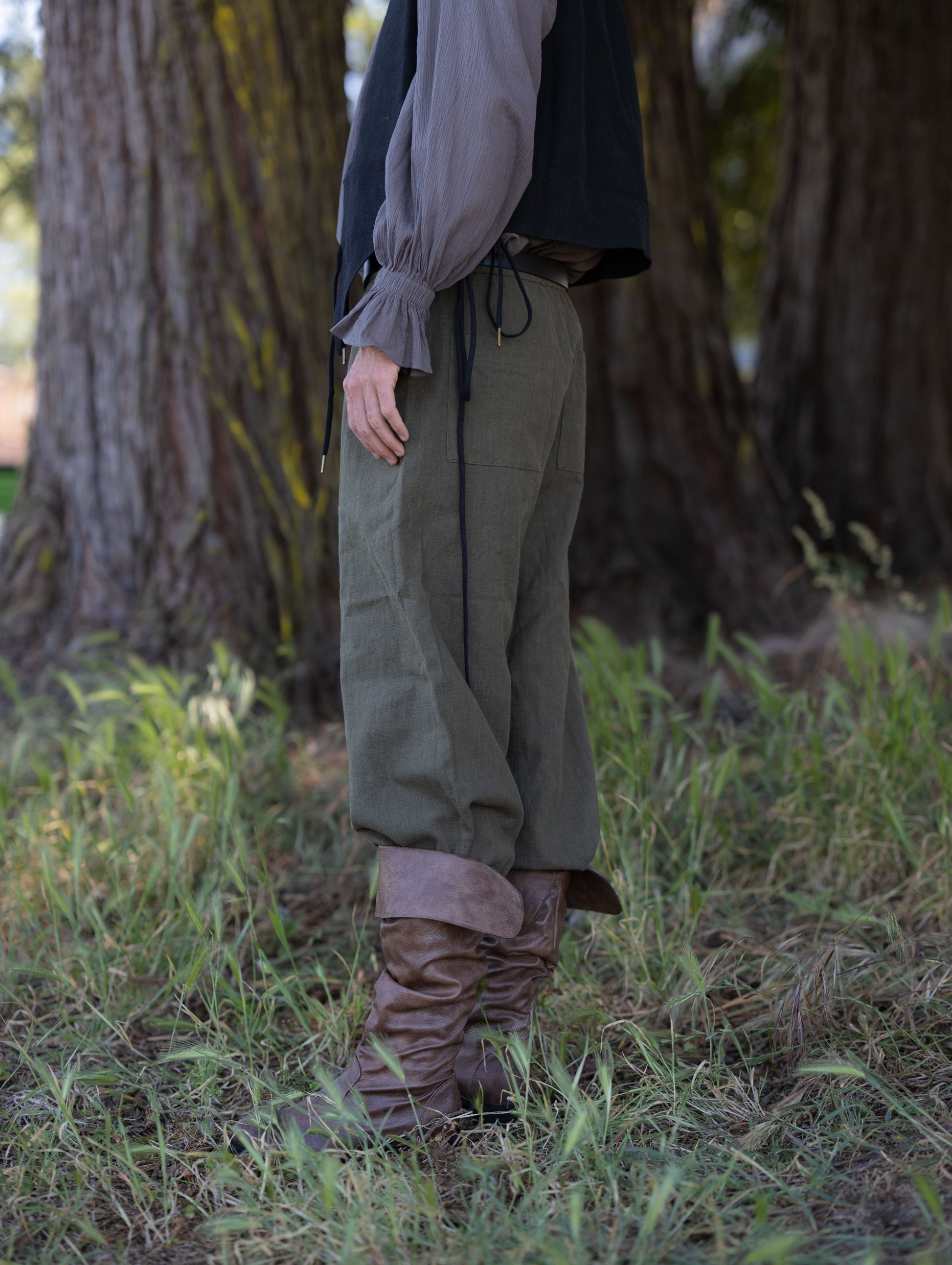 Side view of rustic green pirate pants made from soft ramie fabric paired with leather boots outdoors