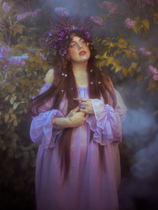 Woman wearing a flowing lilac chiffon chemise with puff sleeves amidst ethereal garden foliage and mist.
