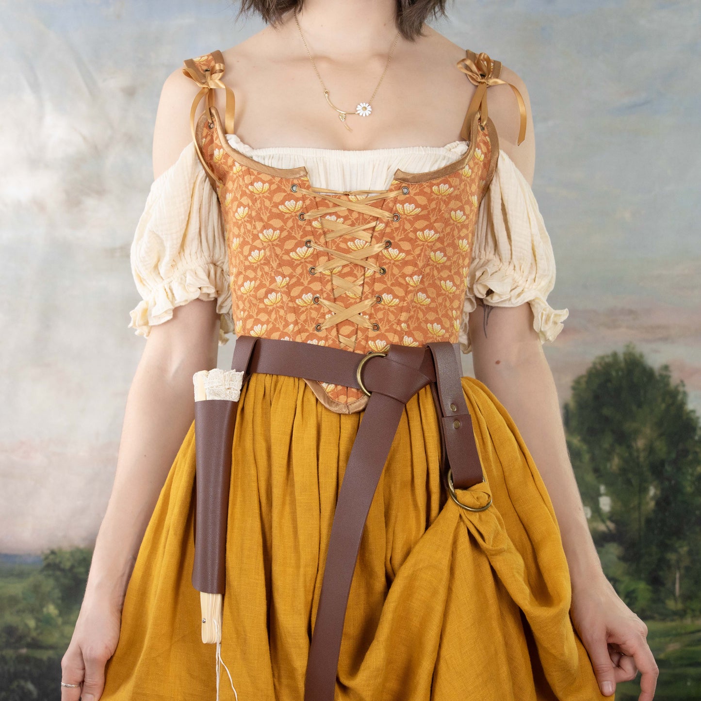 Woman wearing a Handmade Orange Floral Jacquard Corset with puffed sleeves, mustard skirt, and leather belt accessories
