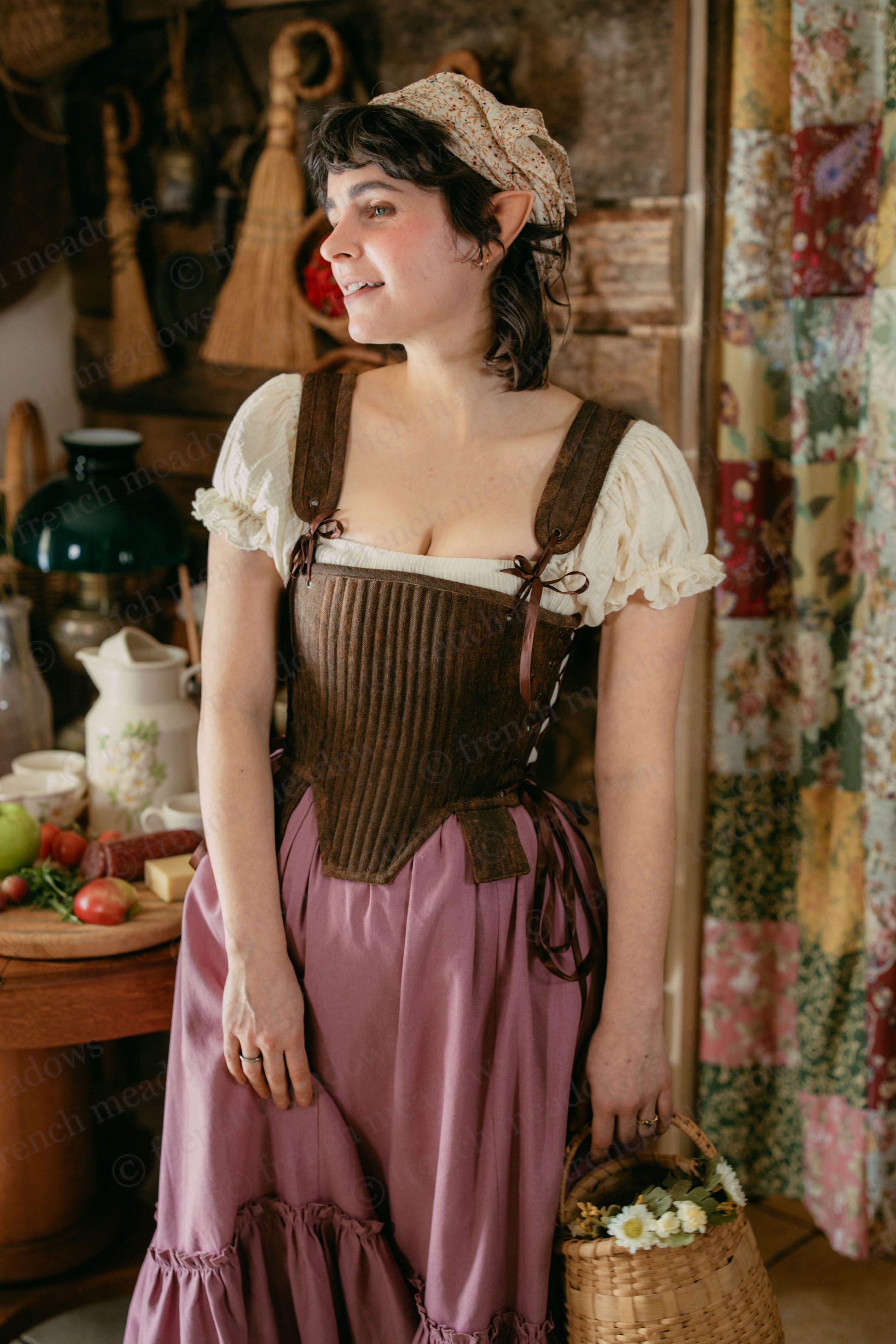 Brown Tabbed Tudor Stays shown with cream blouse and rose skirt in rustic kitchen setting, displaying historical corset design