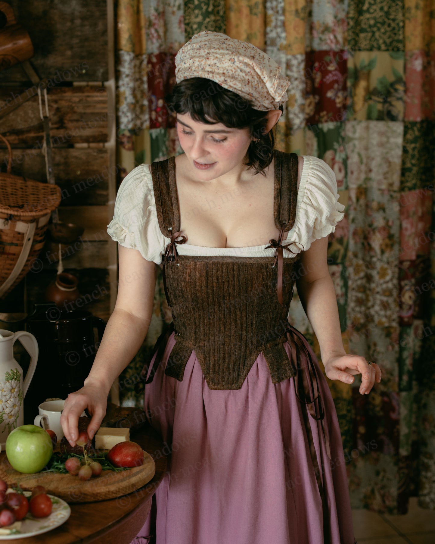 Brown Tabbed Tudor Stays shown on model wearing historical costume with white chemise and pink skirt, preparing fruits in rustic setting