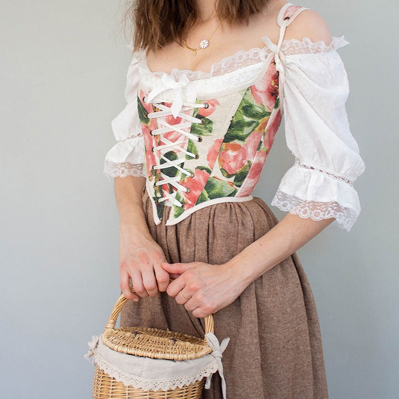 Handmade Pink Peony Renaissance Bodice with floral print, white lace sleeves and brown skirt, shown with wicker basket