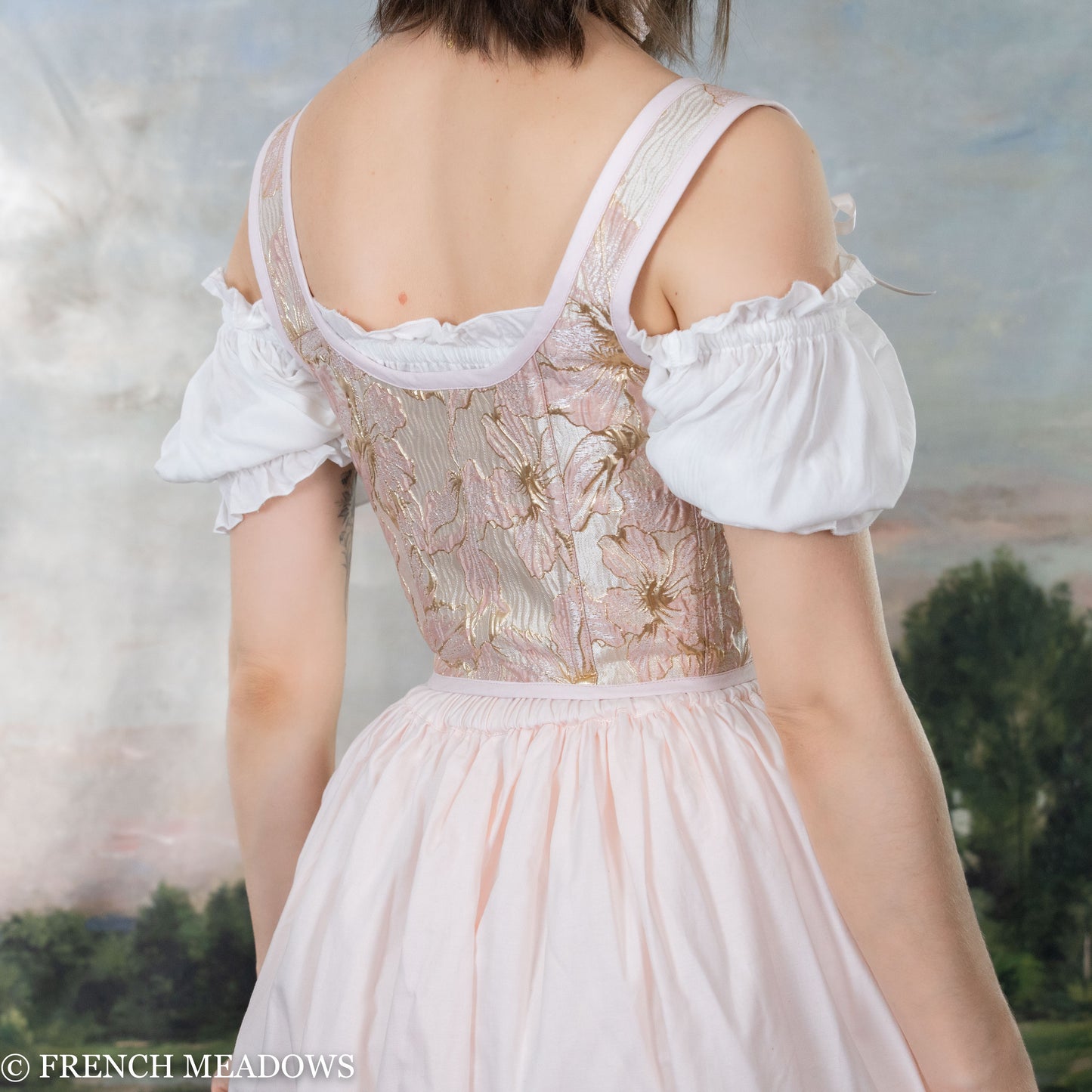 Pink and metallic gold floral Renaissance bodice with off-shoulder white sleeves, shown from back view against pastoral backdrop