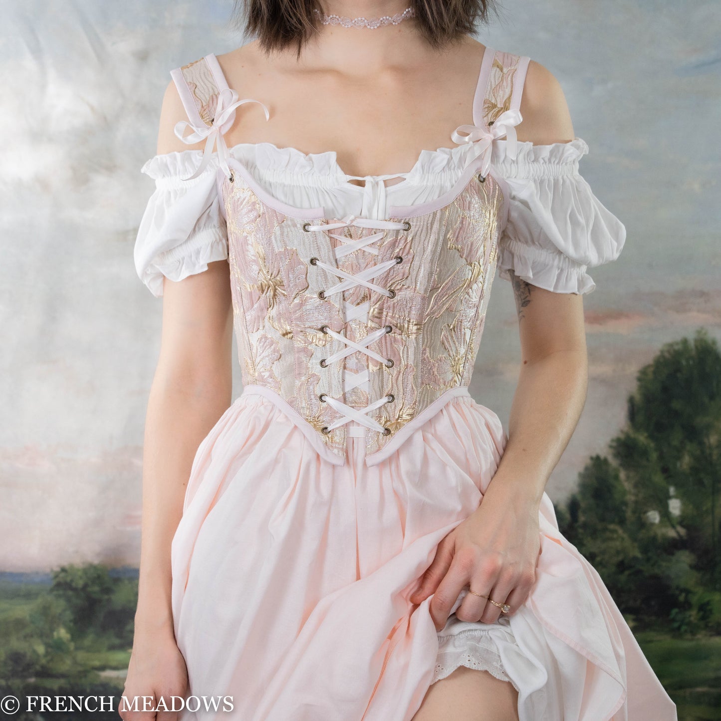 Pink and metallic gold floral Renaissance bodice with lace-up front and off-shoulder white sleeves shown against pastoral background