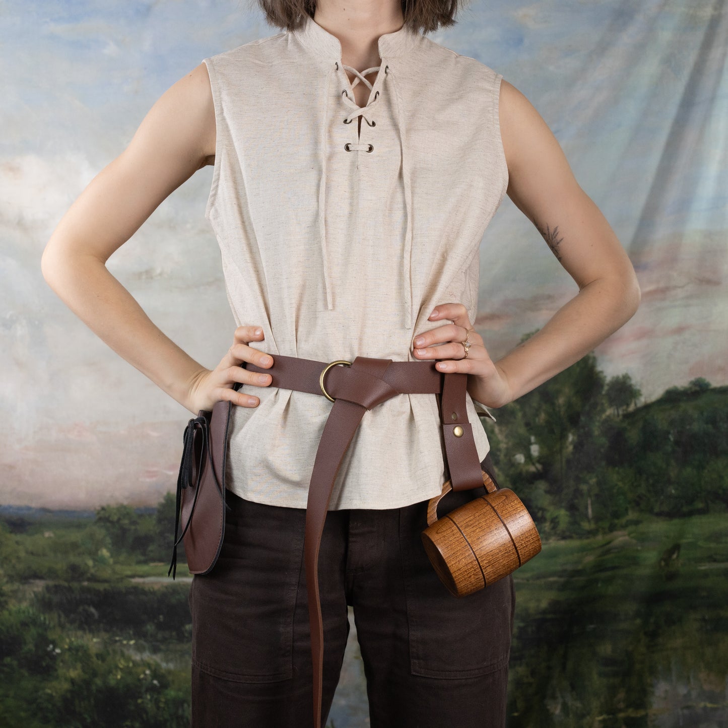 Linen Sleeveless Pirate Tank in natural heather with lace-up neckline and brown leather belt against pastoral backdrop
