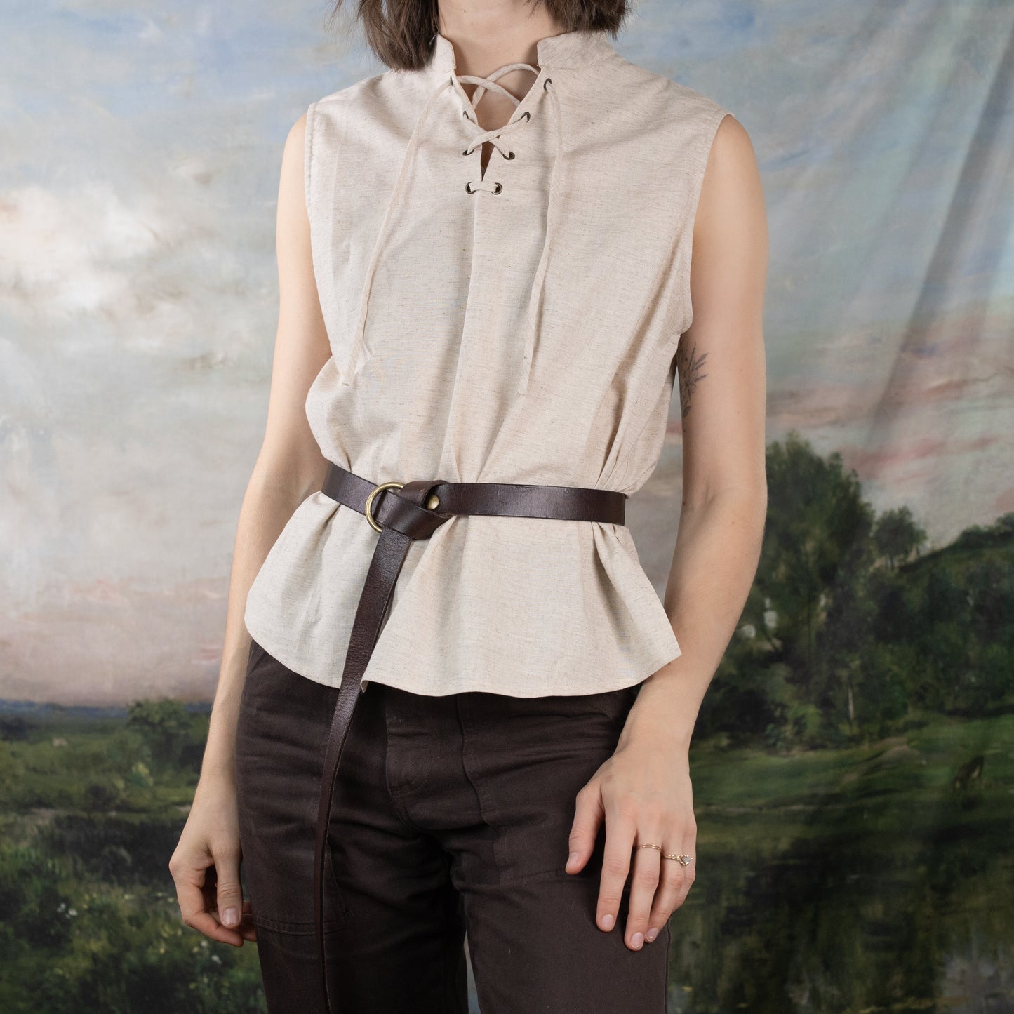 Linen Sleeveless Pirate Tank shown with lace-up neckline and leather belt, styled on rustic landscape background