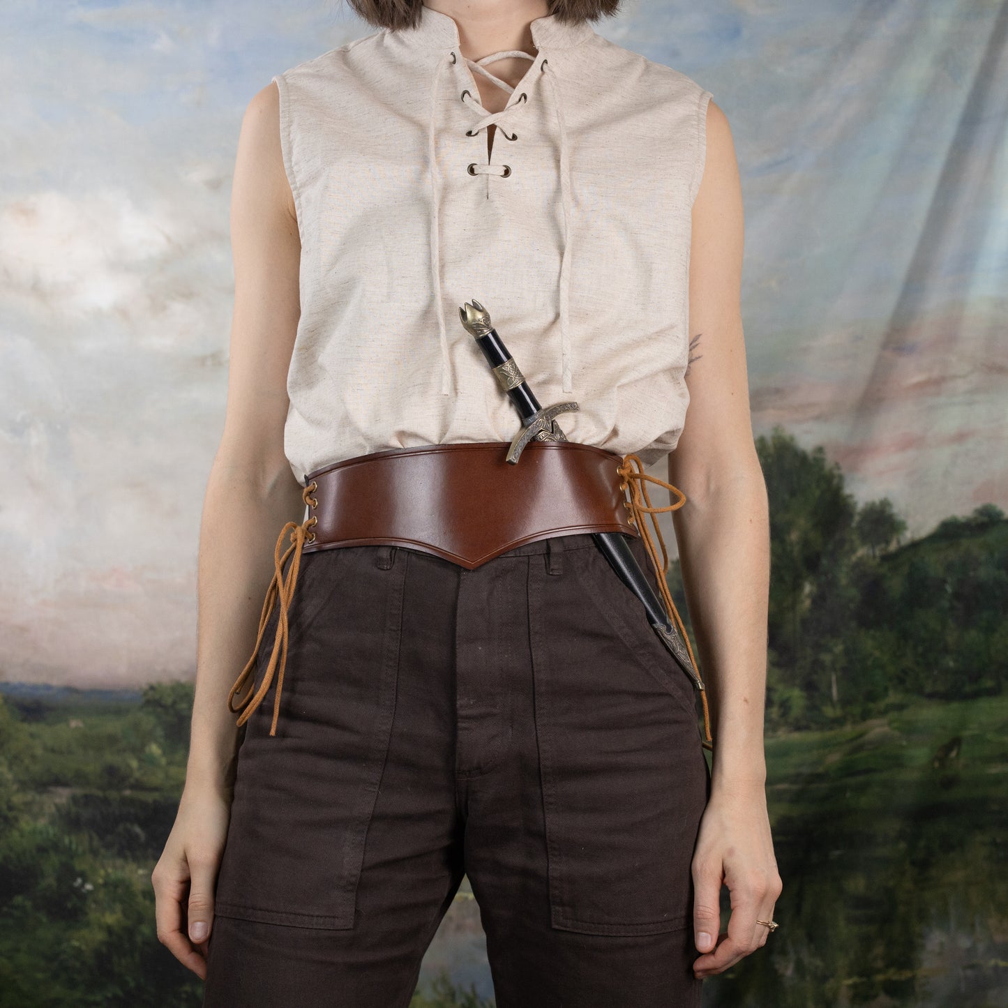 Linen Sleeveless Pirate Tank in natural heather with lace-up neckline and brown leather belt against scenic backdrop