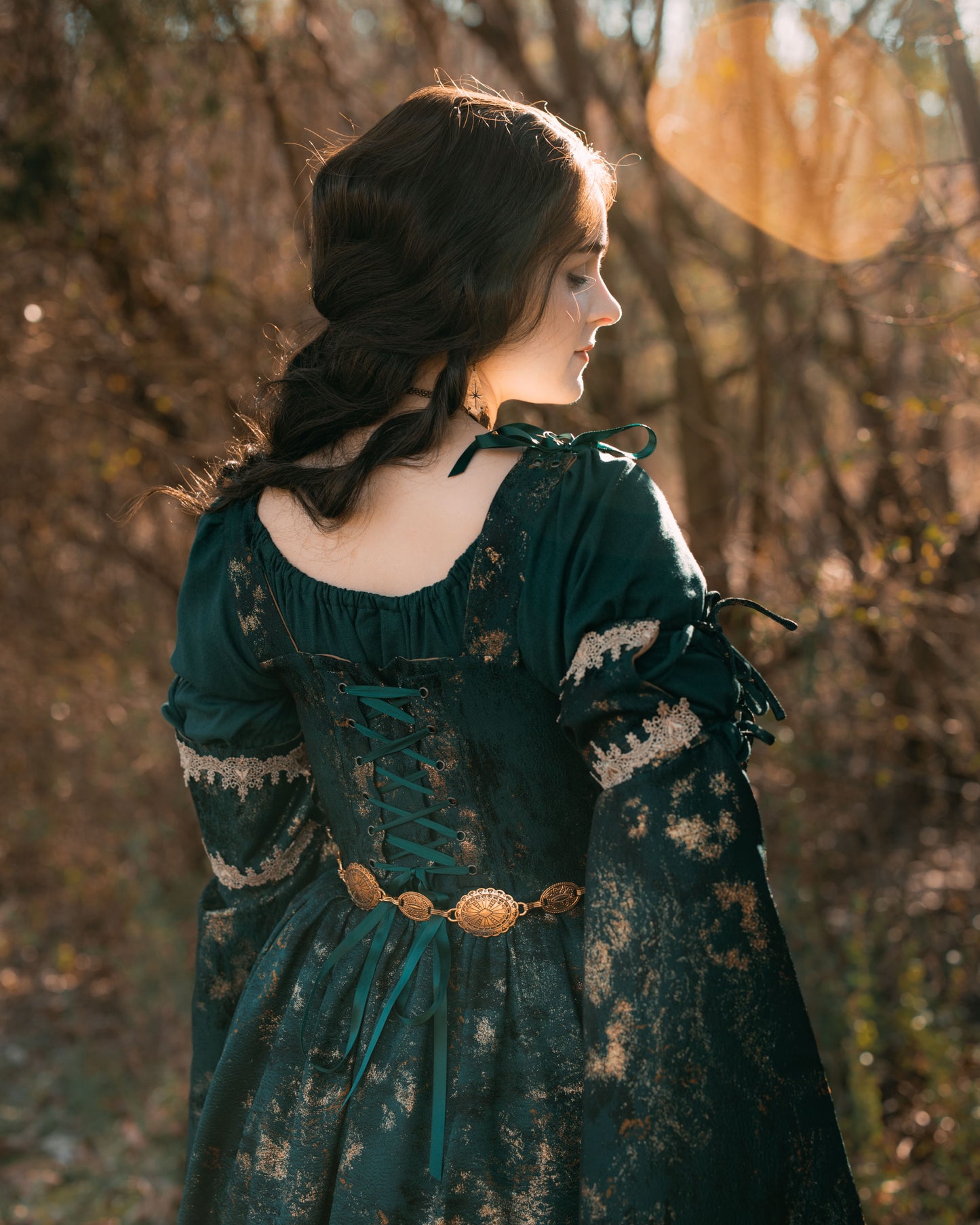 Dark green jacquard corset dress with gold trim and bell sleeves shown outdoors in warm autumn sunlight, back view detail
