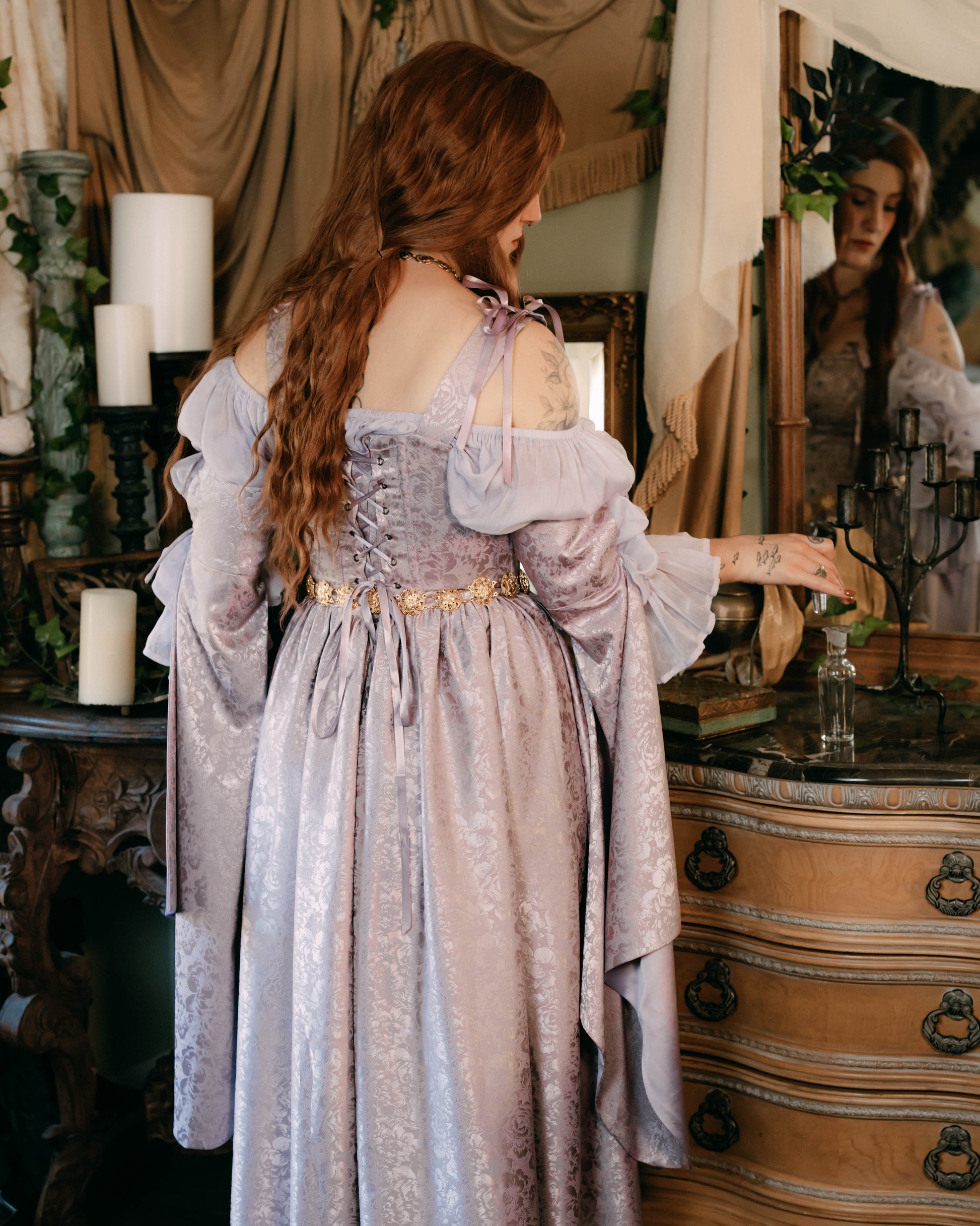 Lavender floral satin corset dress with lace-up back and bow-tied straps shown from behind in romantic vintage setting
