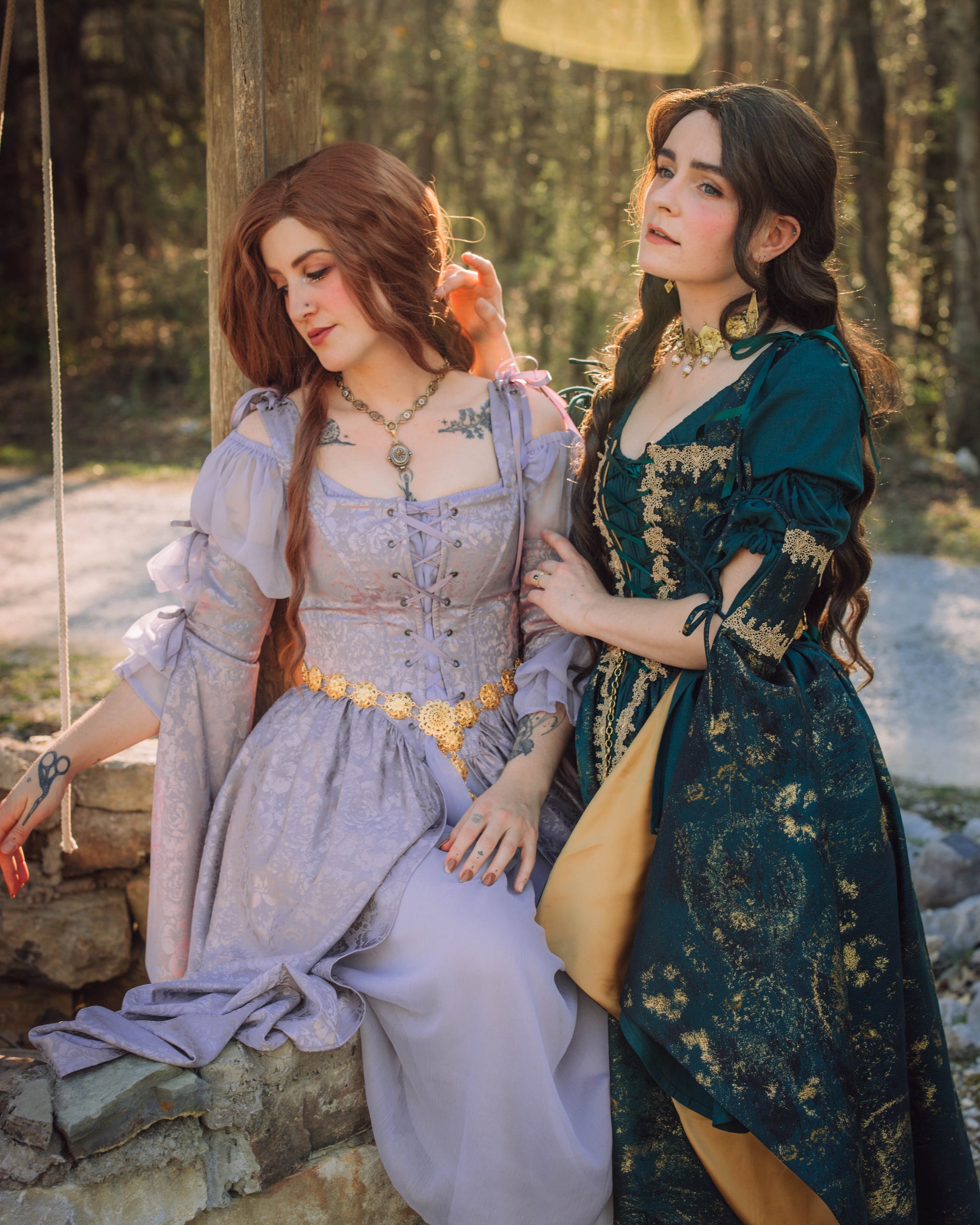 Lavender Floral Satin Corset Dress shown in enchanted forest setting alongside emerald dress, displaying romantic medieval style