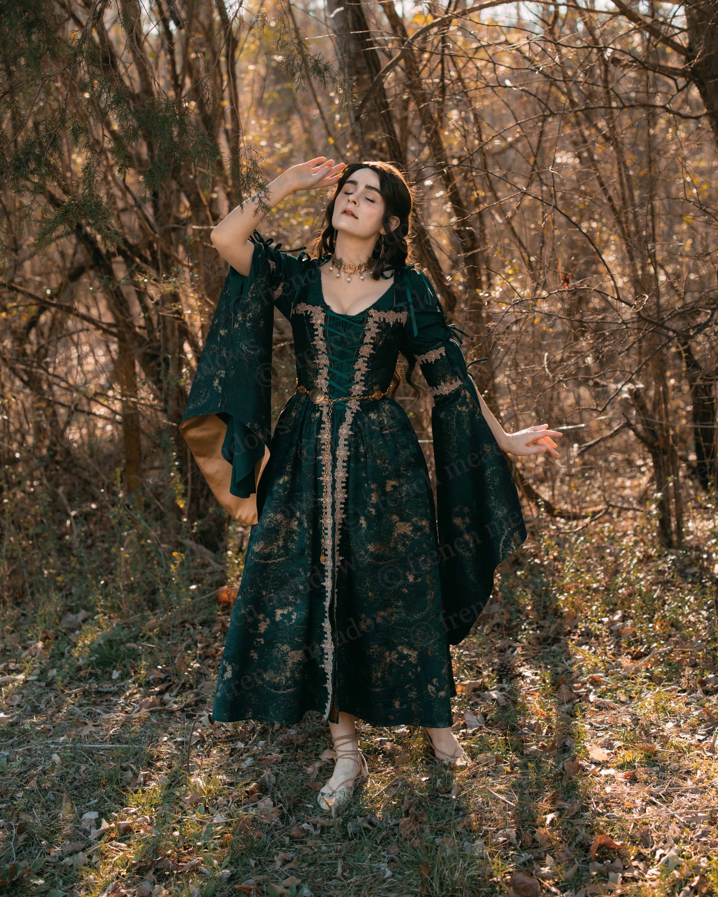 Dark green jacquard corset dress with gold trim and bell sleeves shown in autumn forest setting with dramatic lighting