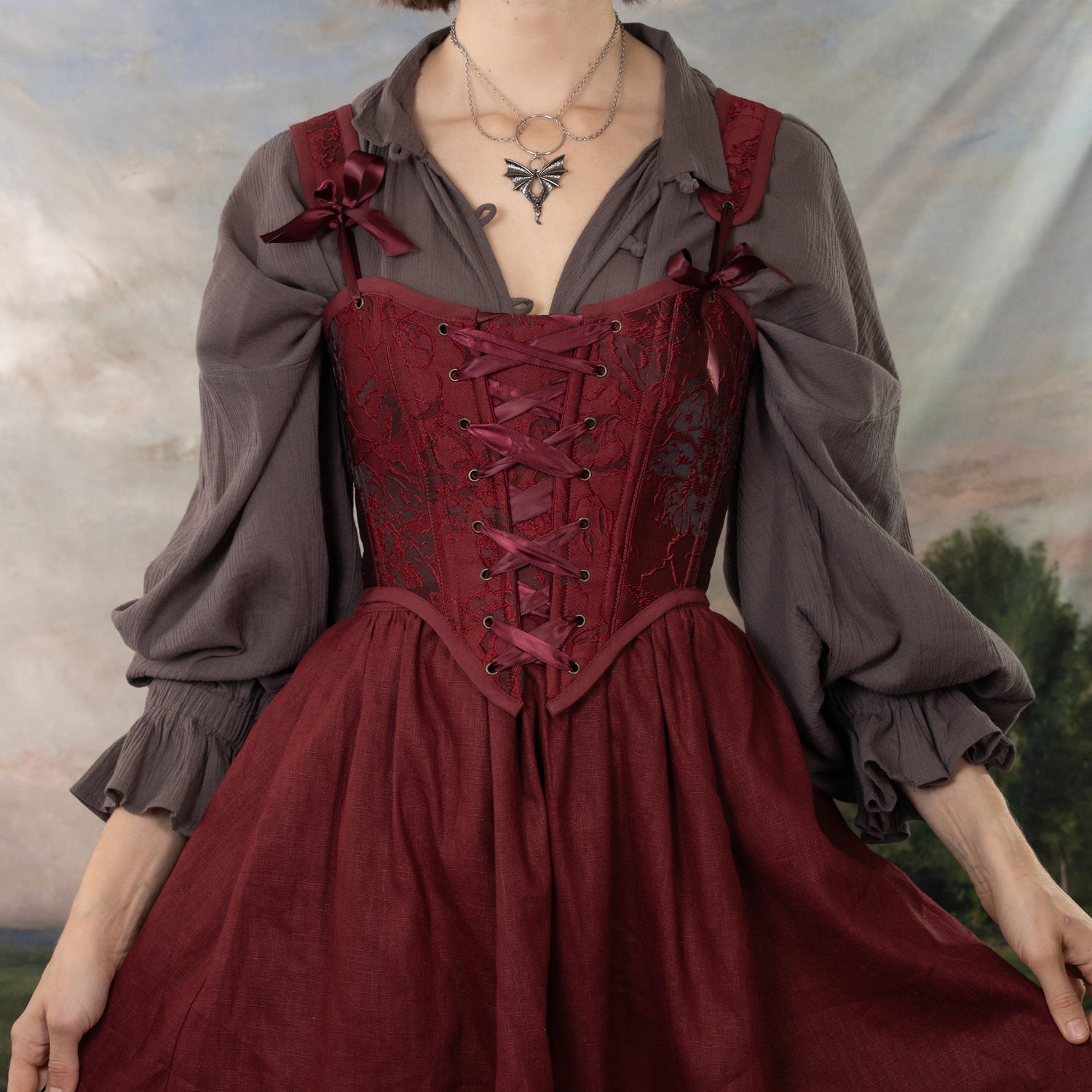 model wearing dark red corset with matching skirt and grey poet blouse