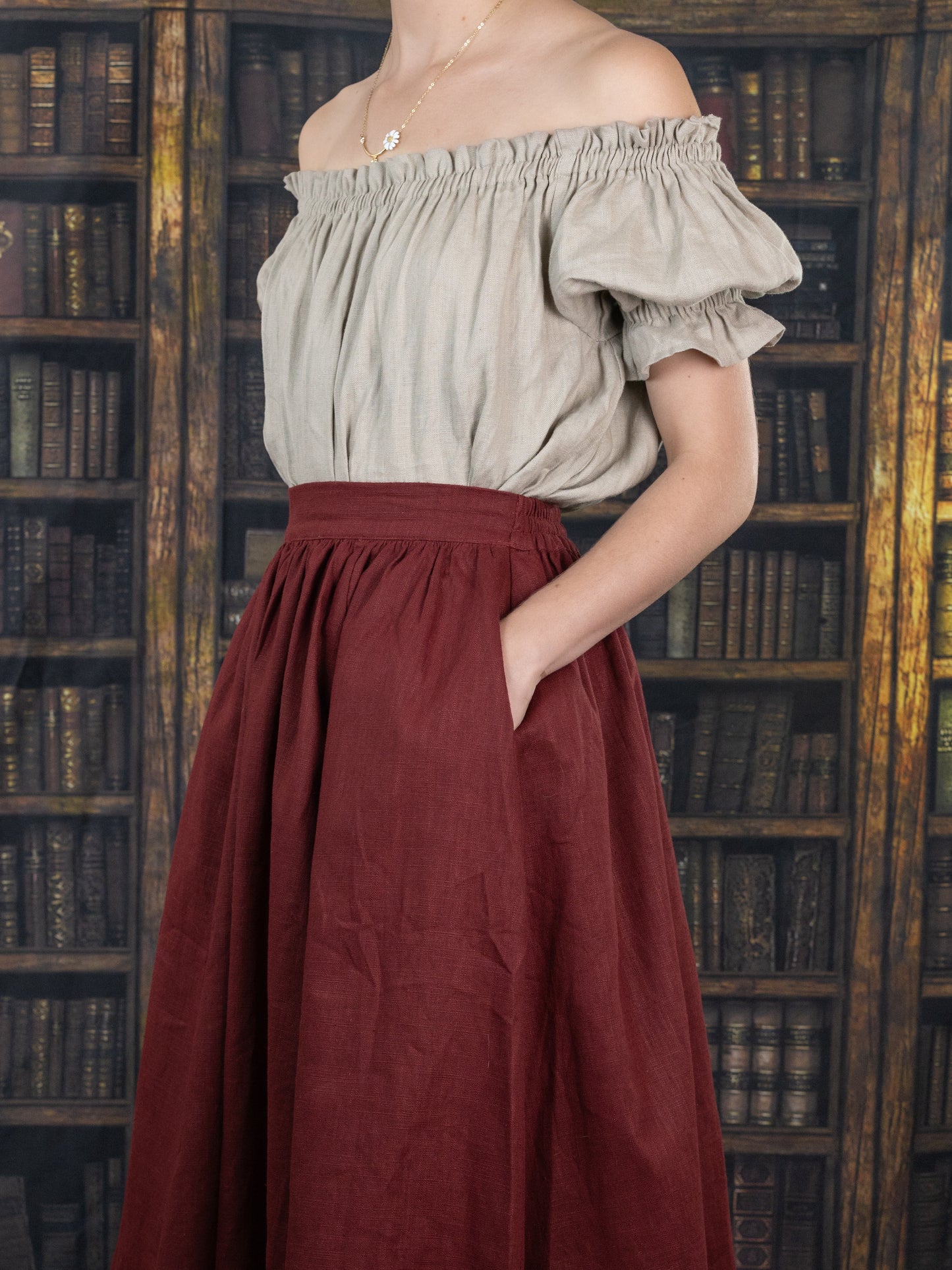 Burgundy Ramie Midi Skirt shown with off-shoulder peasant top in library setting, featuring gathered waist and side pockets