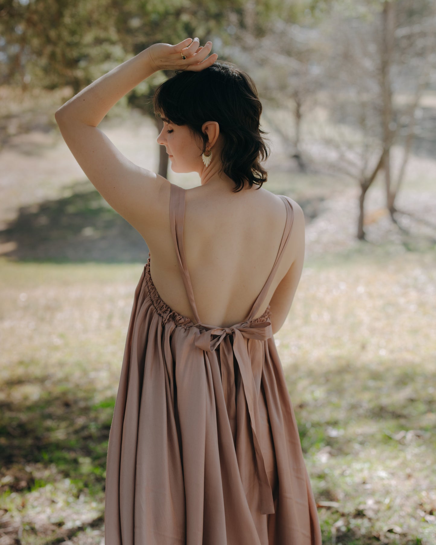 Woman wearing a loose low-back Flutter Fairy Dress with adjustable straps outdoors in a sunlit garden setting.