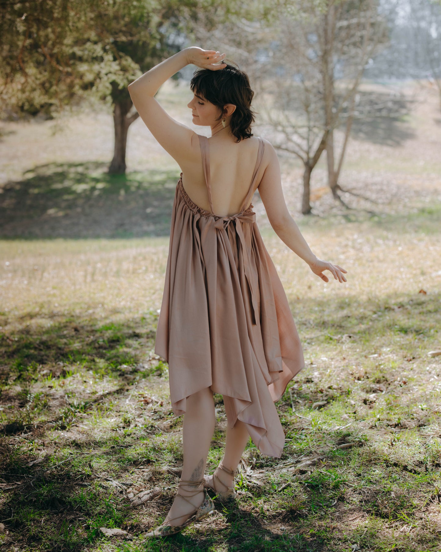Woman outdoors wearing a low-back, handkerchief hem Flutter Fairy Dress with adjustable straps in nature setting.