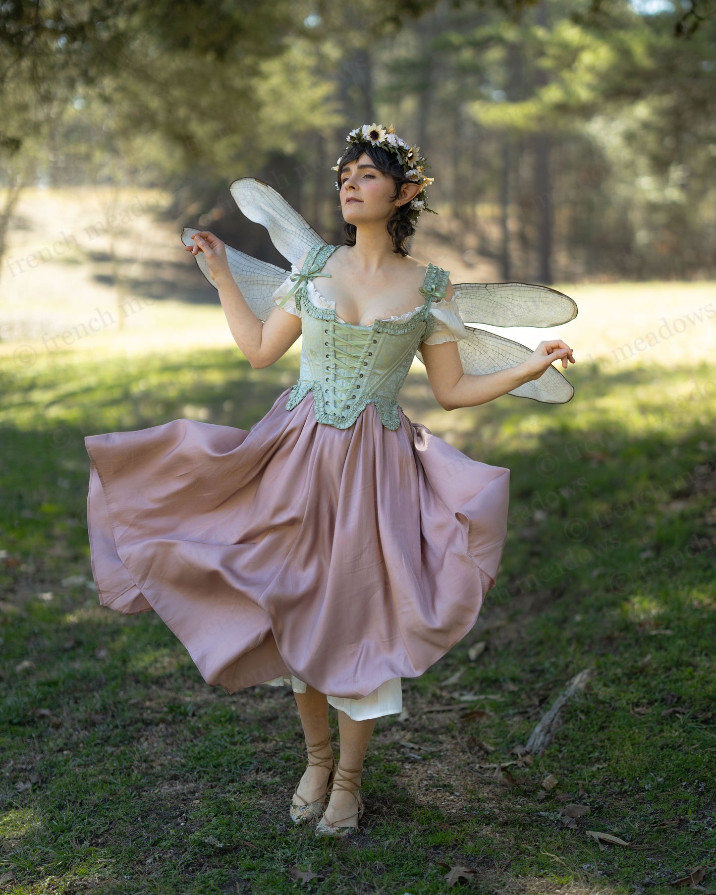 Woman wearing a flowing Flutter Fairy Dress with handkerchief hem and floral accents in a forest setting