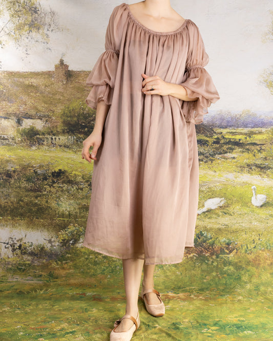 Woman wearing a soft muted rose dress with puffed sleeves standing in front of a pastoral painting Rose Chiffon Chemise