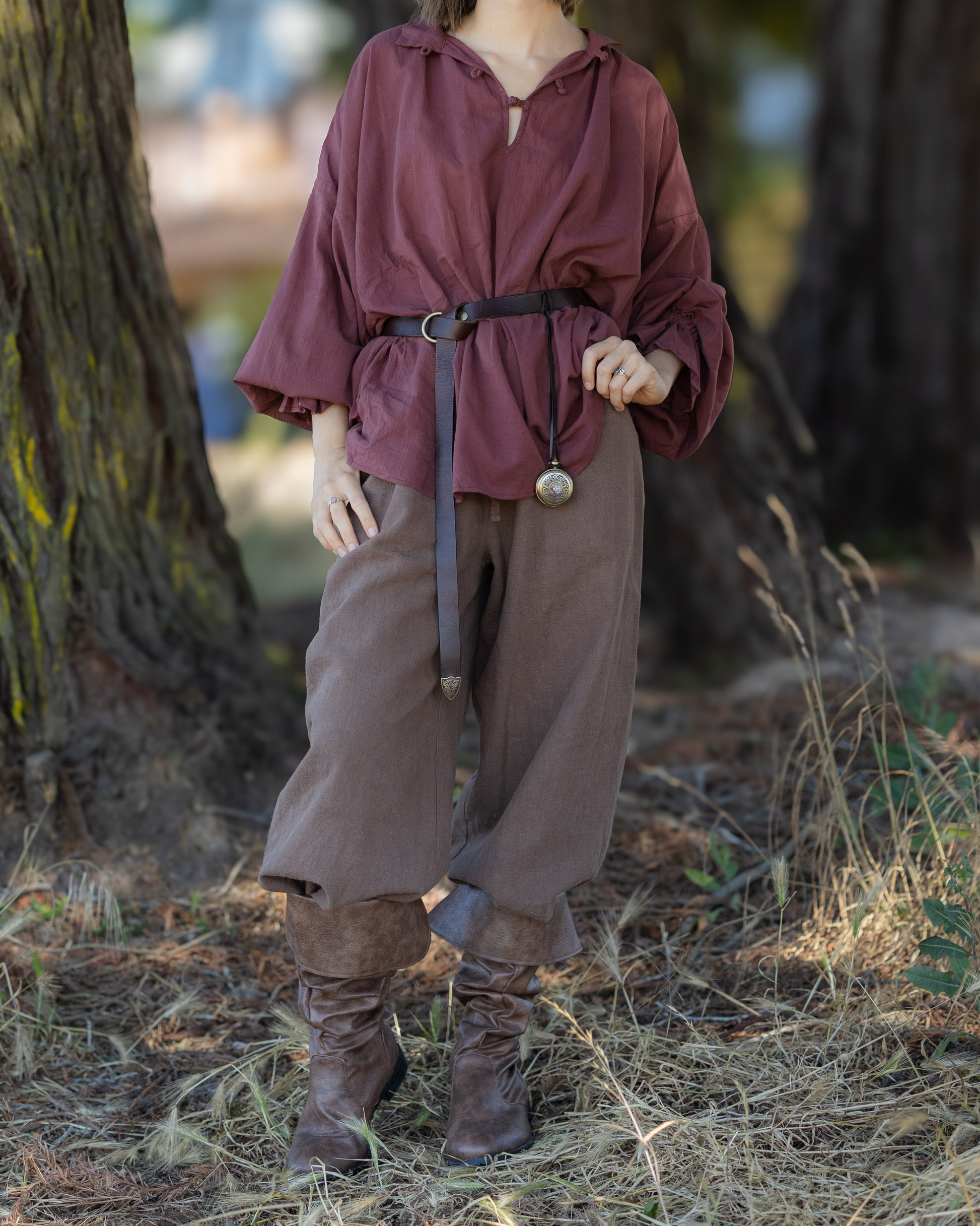 Person wearing a loose brown historic-inspired Darcy Shirt with wide sleeves, belt, baggy pants, and boots outdoors.