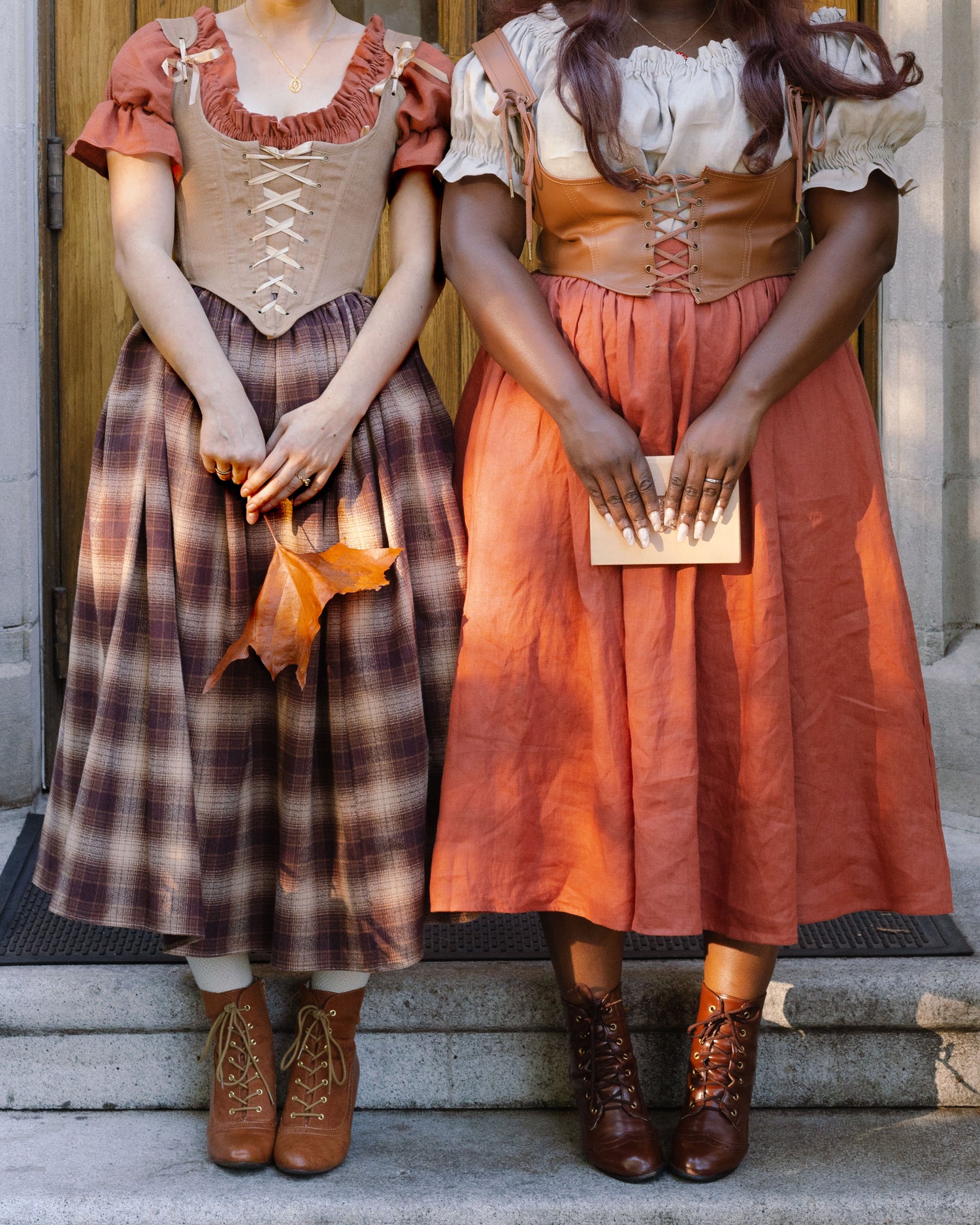 Two renaissance-style outfits featuring corsets and long skirts in plaid and persimmon orange linen with brown lace-up boots