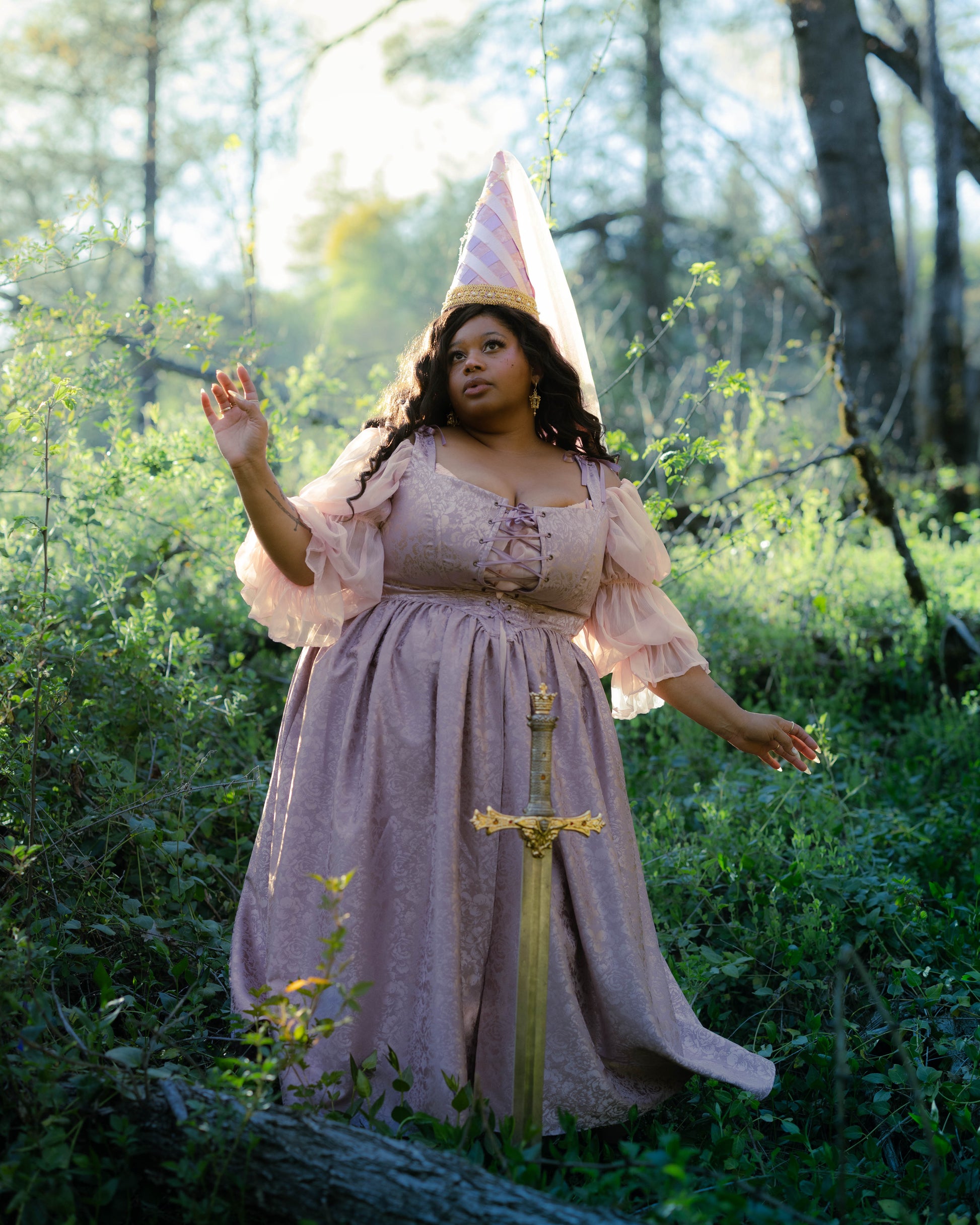 Woman wearing lavender floral satin corset dress with puffed sleeves and square neckline in a sunlit forest setting