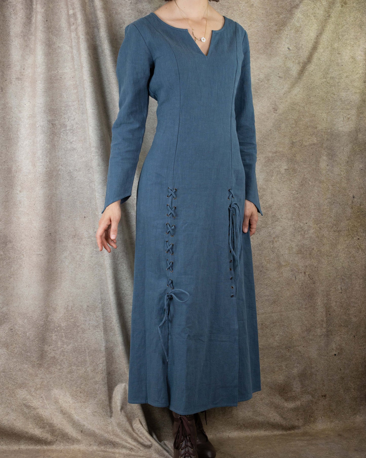 Teal Viking dress with fitted silhouette, pointed sleeves and front lacing detail shown on mannequin against textured backdrop