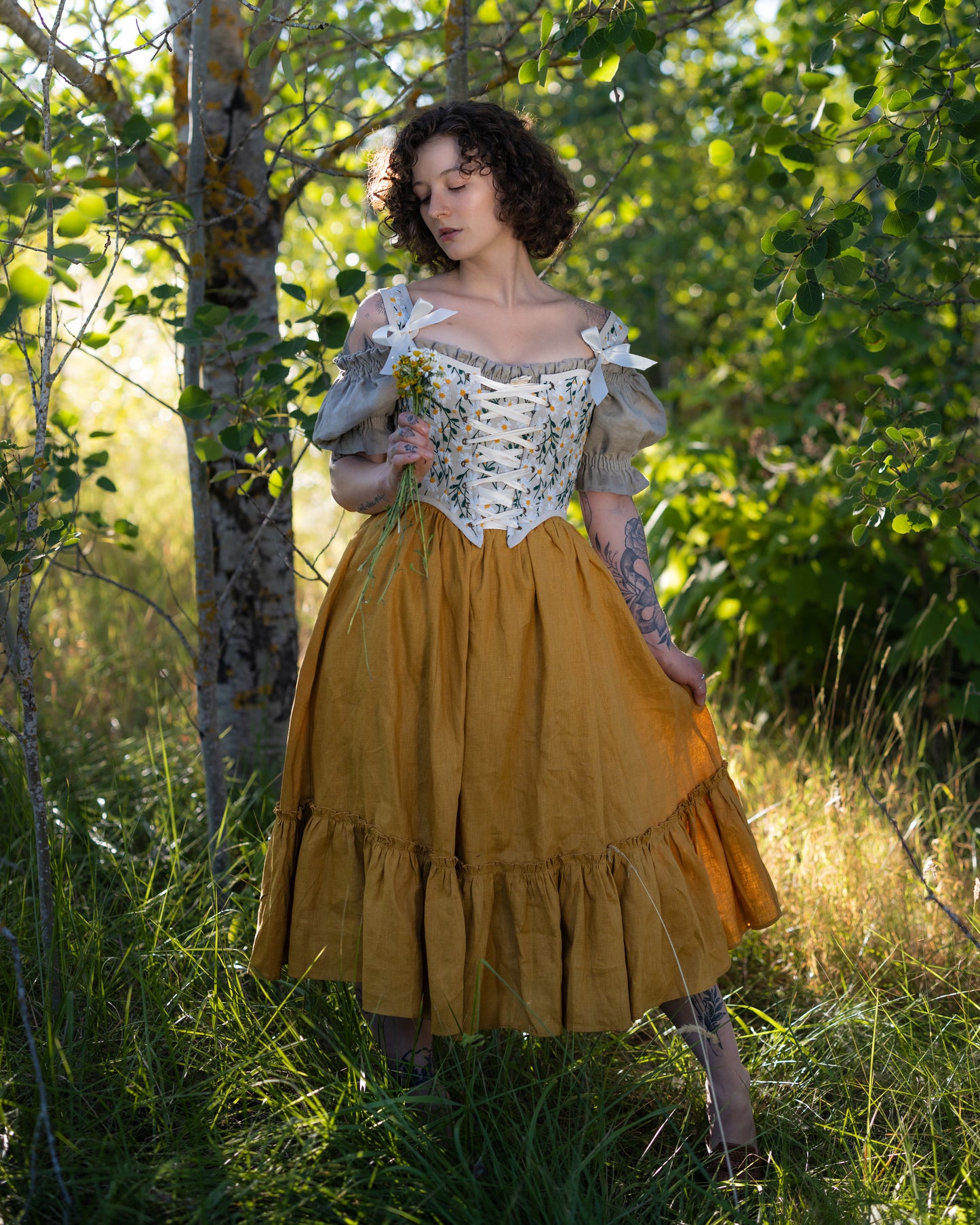 Woman wearing a yellow linen ruffle skirt styled for renaissance faire in a sunlit forest setting