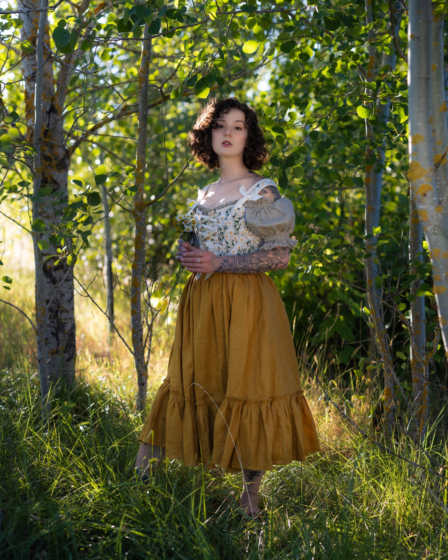 Woman wearing a yellow linen ruffle skirt standing in a sunlit forest setting with trees and grass around her