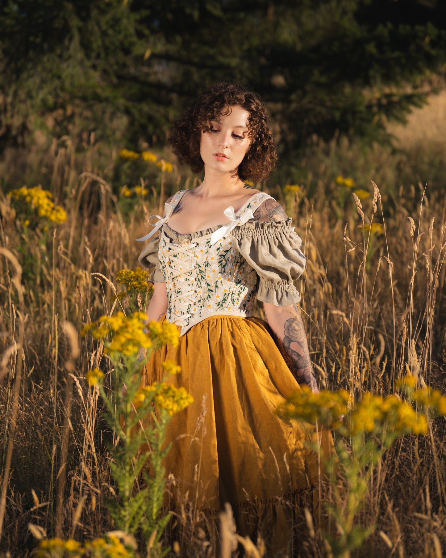Woman wearing a yellow linen ruffle skirt and corset in a field of tall grass and wildflowers at golden hour