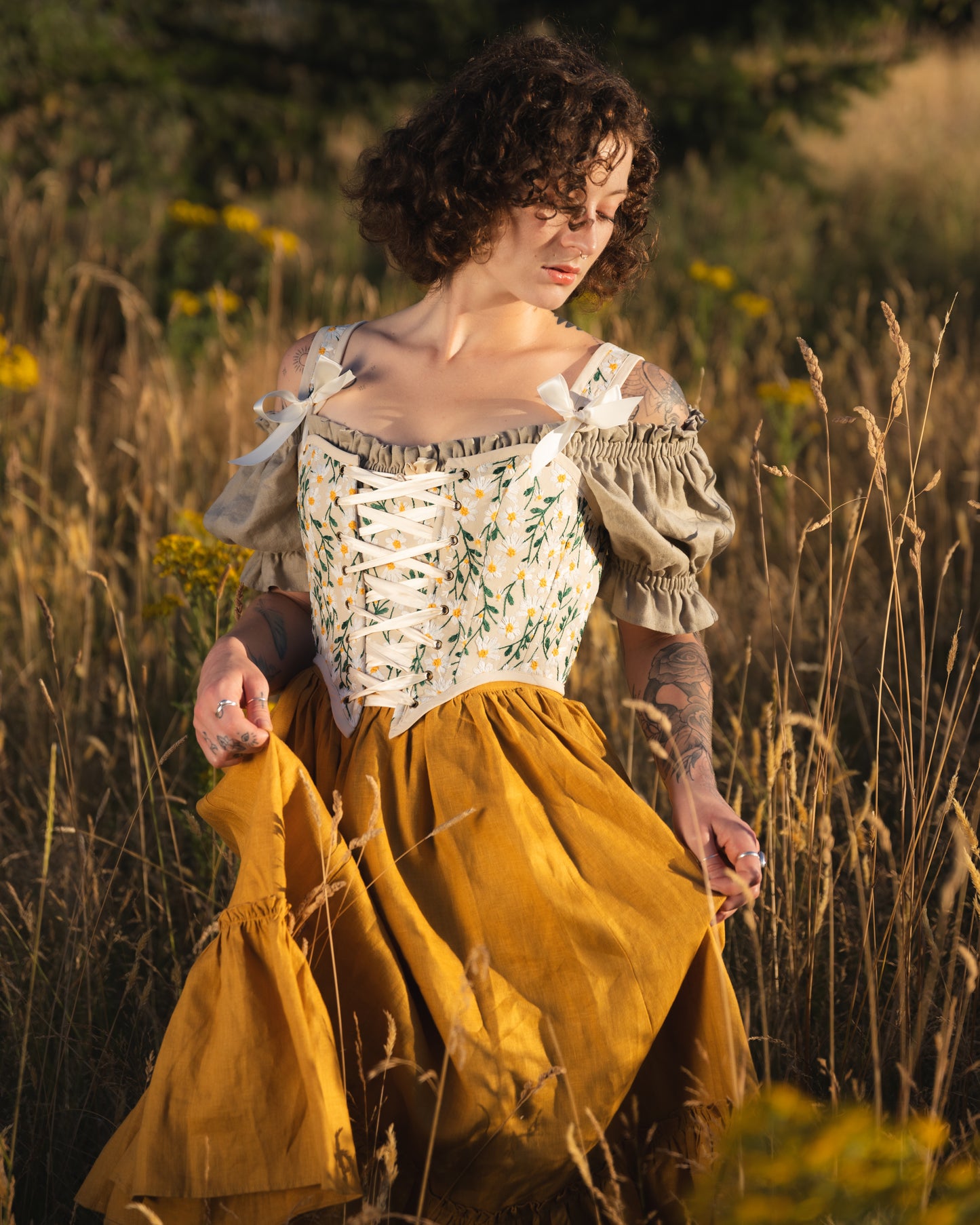 Woman wearing a yellow linen ruffle skirt and embroidered corset standing in a sunlit wildflower field