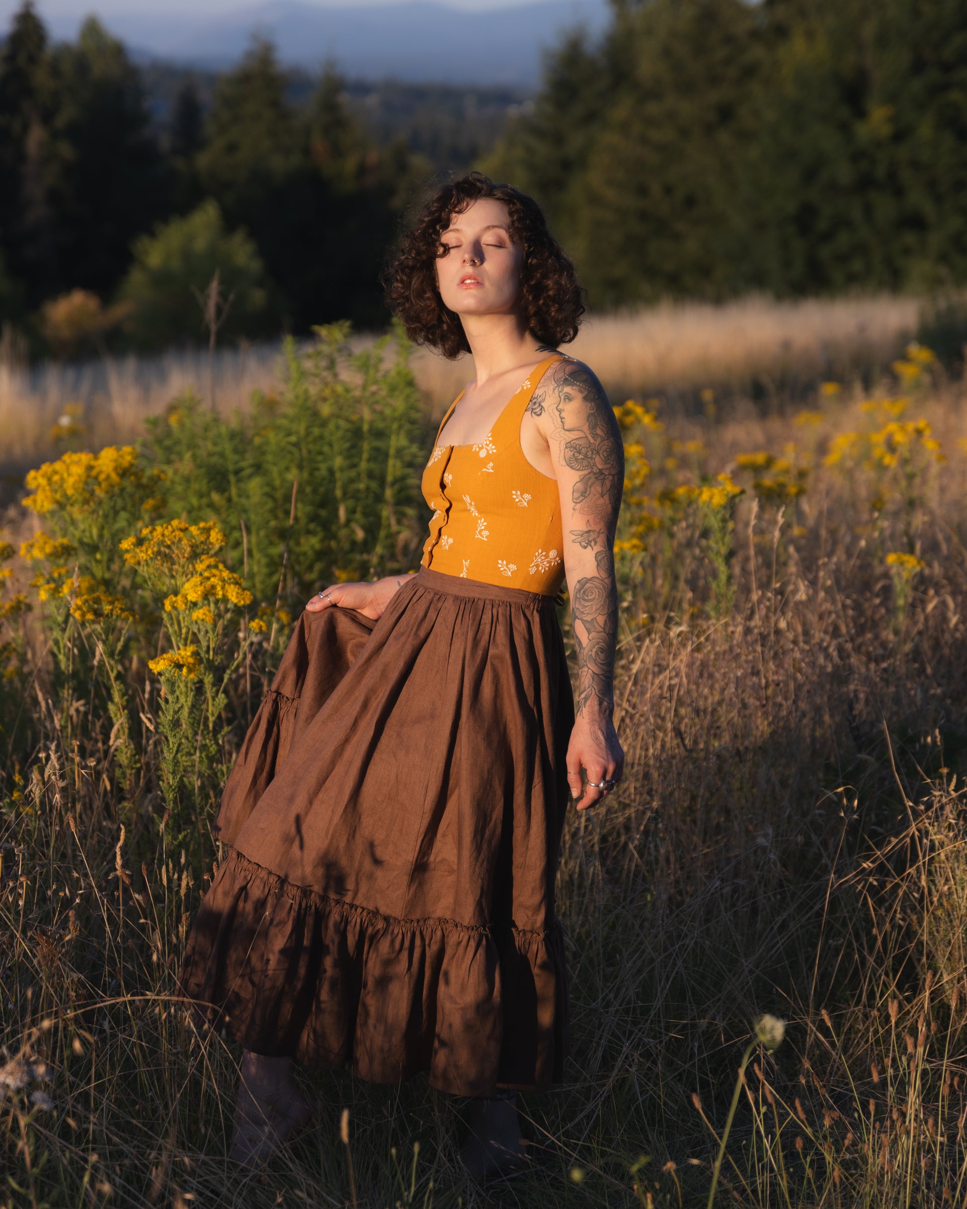 Brown Linen Ruffle Skirt shown in outdoor meadow setting with golden wildflowers at sunset, paired with yellow floral top