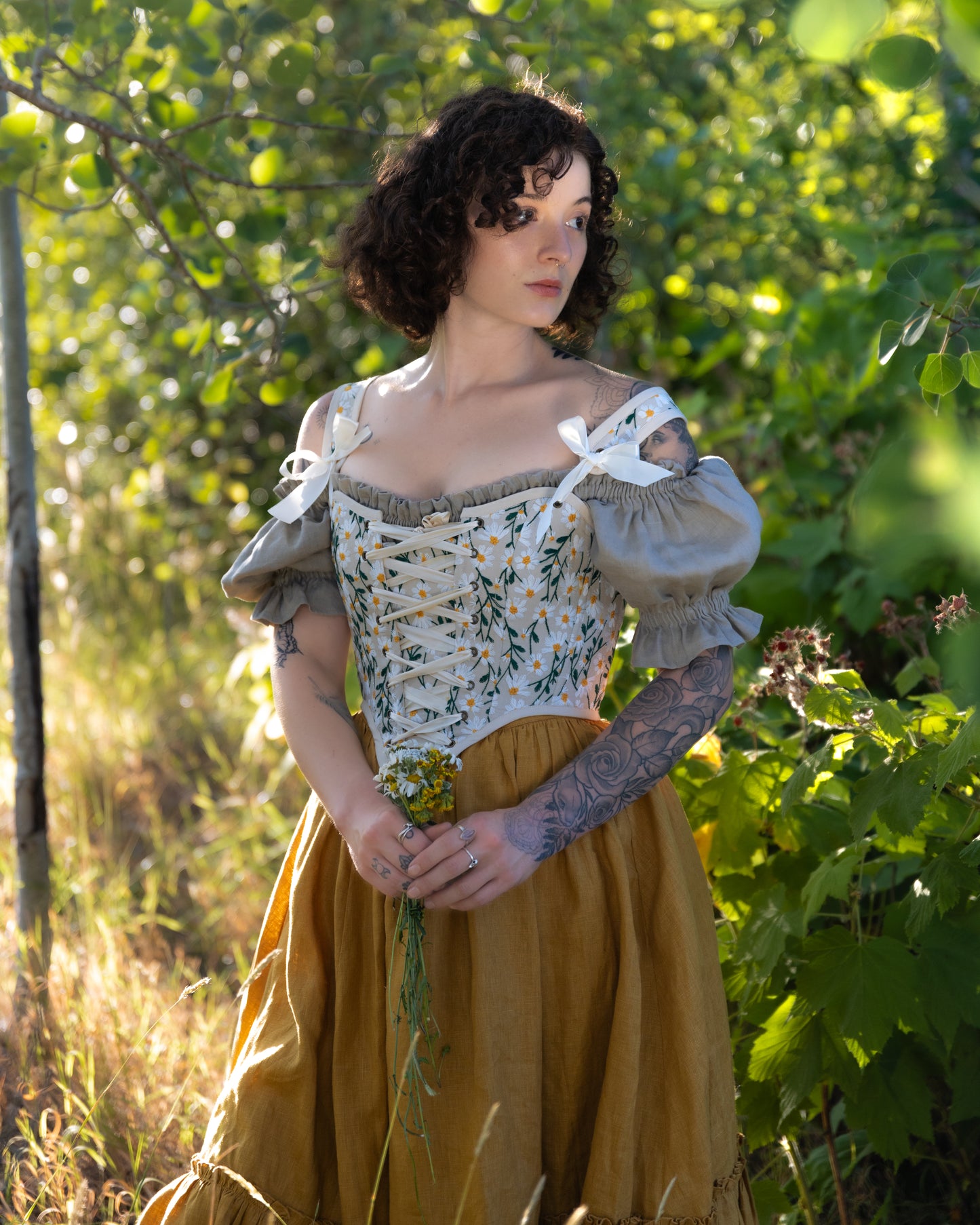 Embroidered Daisies Corset Top with floral design and puffy sleeves, shown outdoors against lush green foliage in natural lighting
