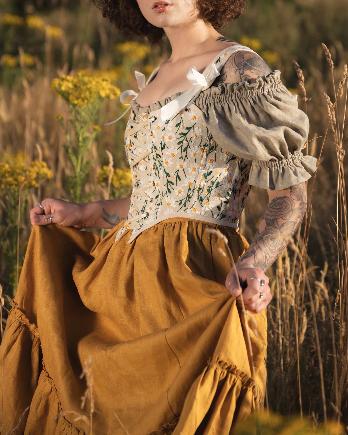Embroidered Daisies Corset Top shown in outdoor setting with floral embroidery and puff sleeves against golden wildflower field