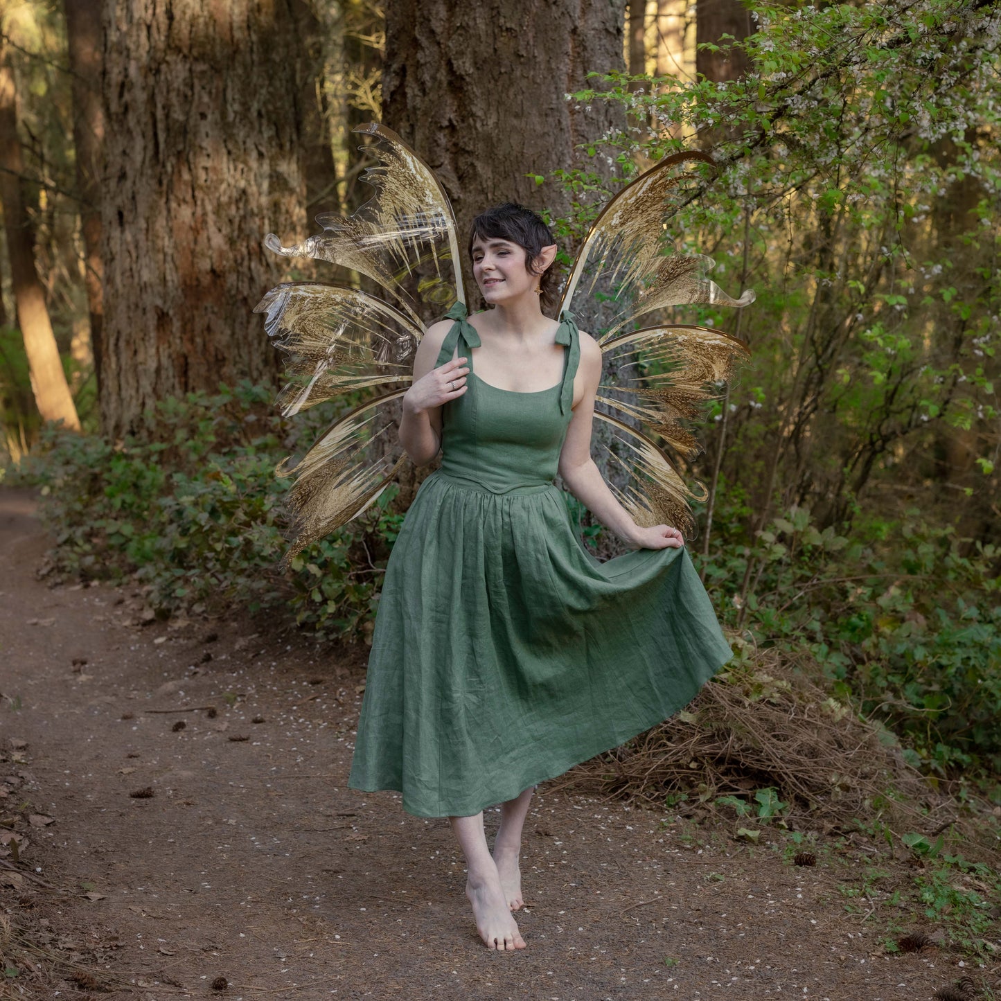 Woman wearing an Ivy Green Linen Midi Skirt standing barefoot in a forest with fairy wings.