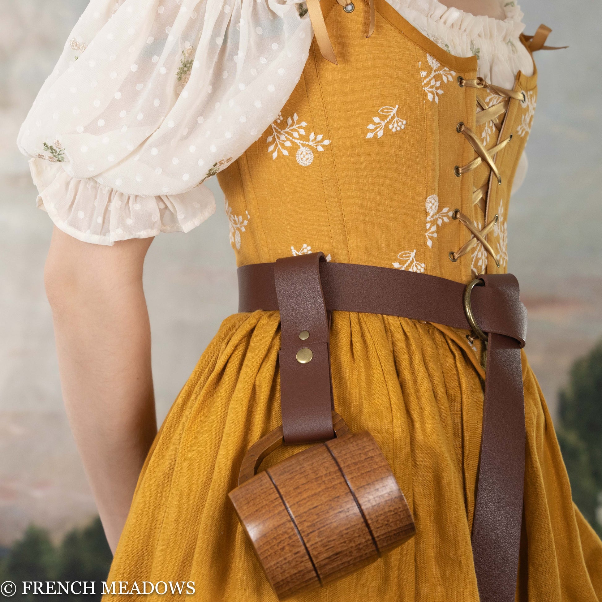 Vegan leather tankard strap attached to brown belt on yellow floral dress, holding wooden mug at waist level
