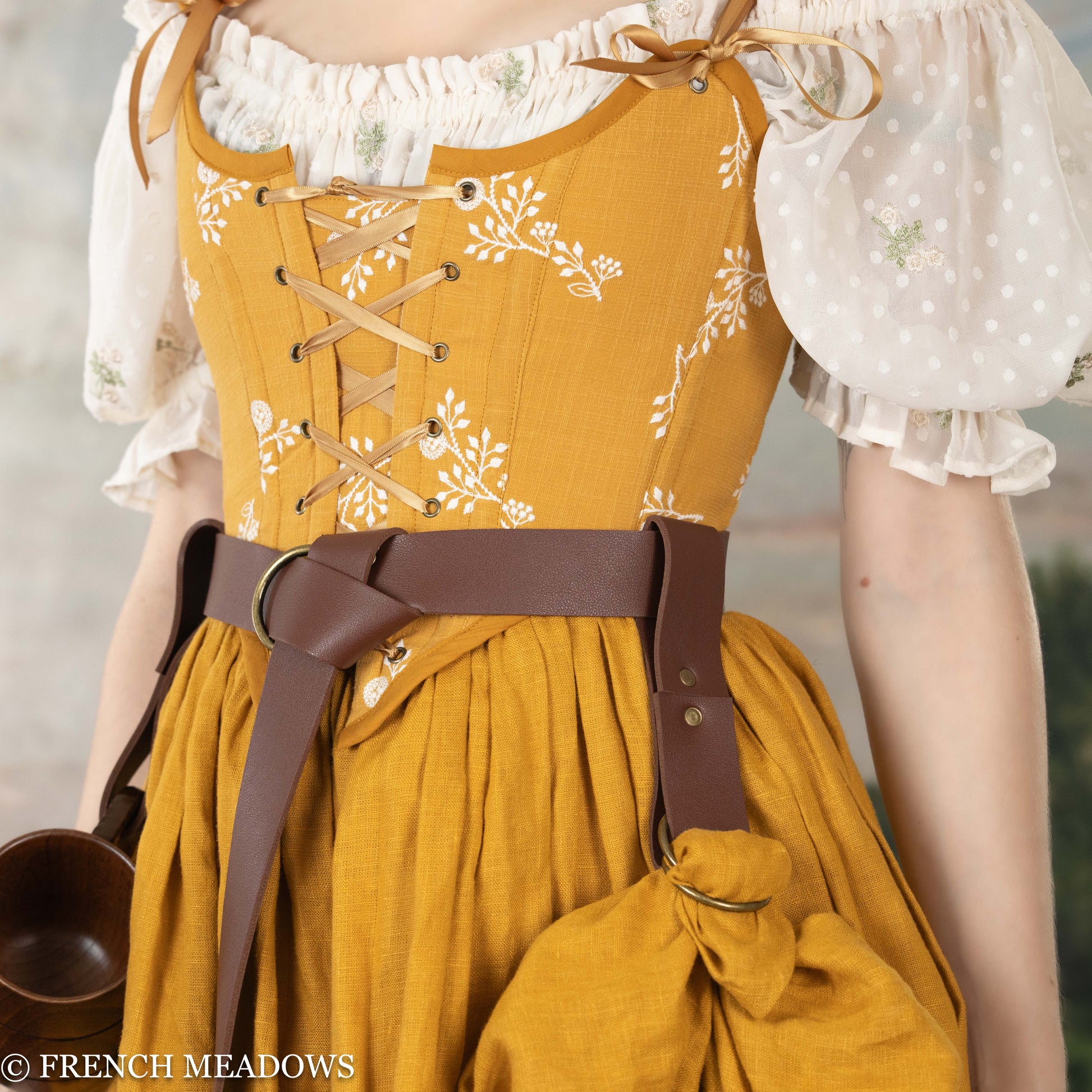 Vegan leather skirt hikes shown on brown belt with yellow floral Renaissance dress and white peasant blouse