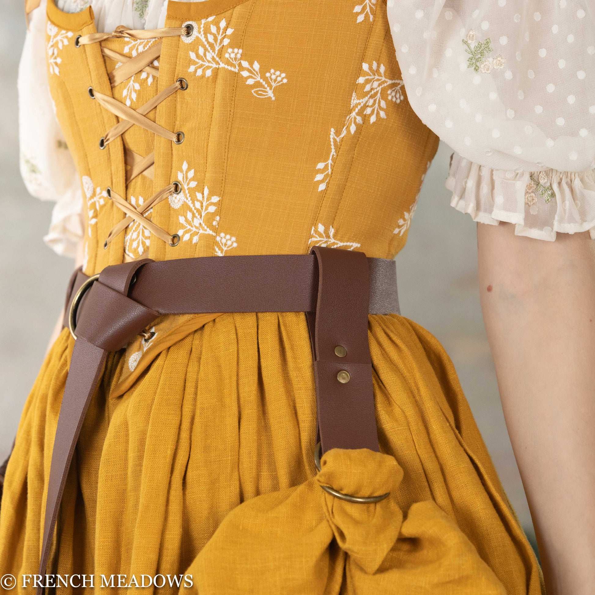 Vegan leather skirt hikes with D-rings shown on brown belt against yellow floral renaissance dress with white blouse