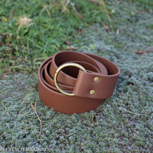 Brown vegan leather renaissance belt with brass ring buckle and rivets displayed on mossy ground