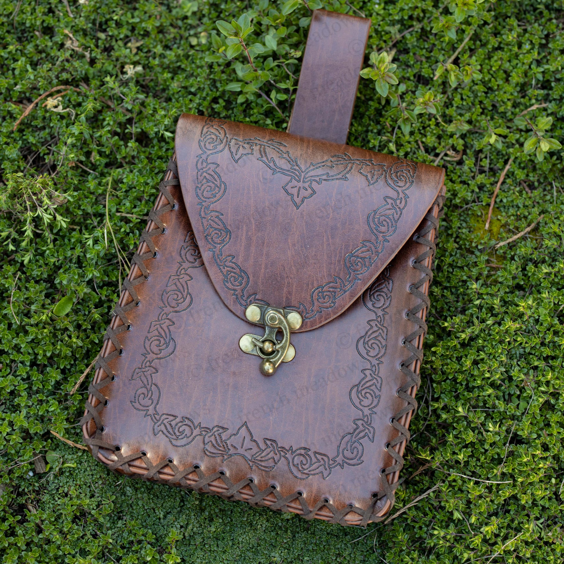 Elven Medieval Belt Pouch with ornate scroll design, brown leather texture, brass clasp, displayed on green grass background