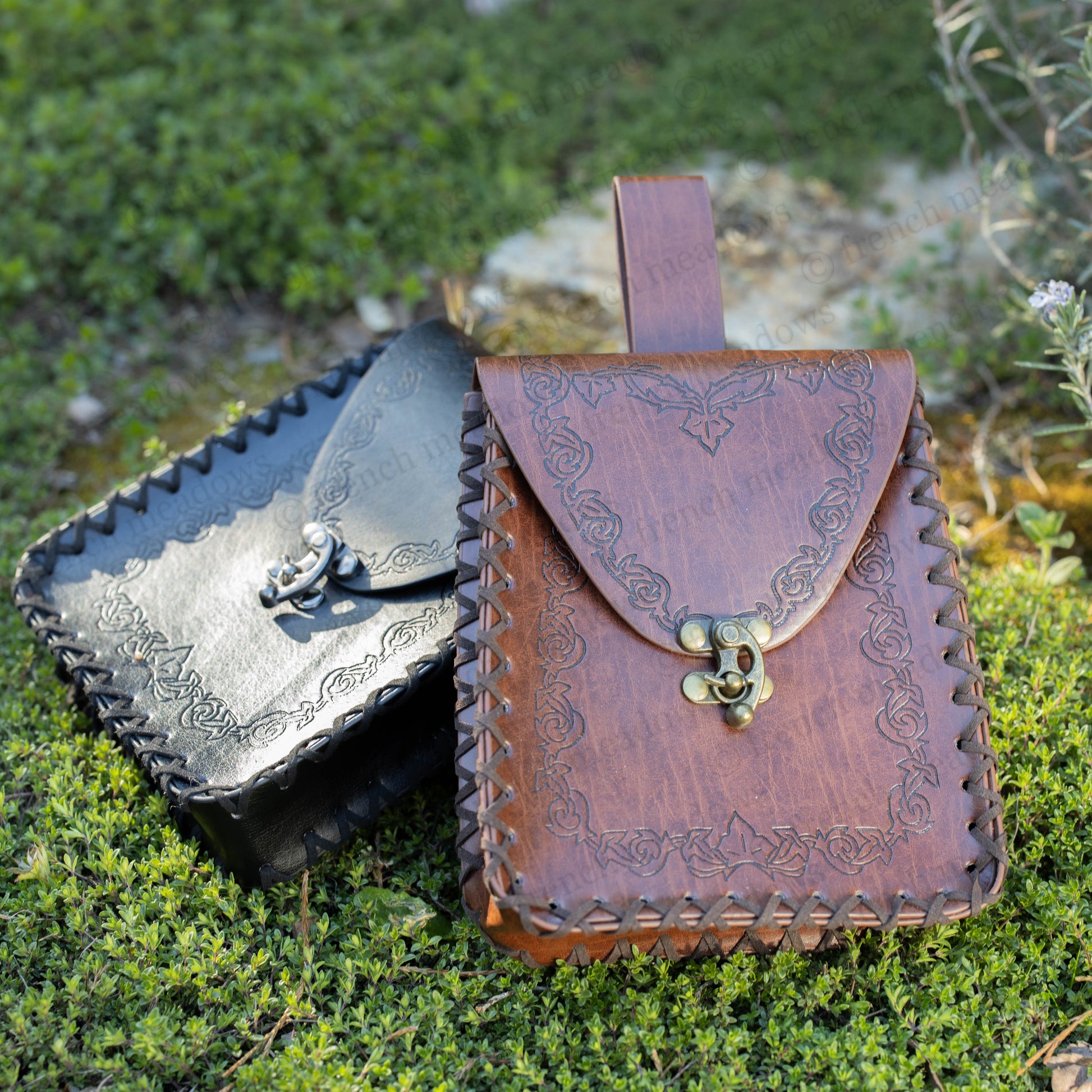 Elven Medieval Belt Pouch in brown and black vegan leather with ornate scroll designs and brass clasp, displayed on mossy ground