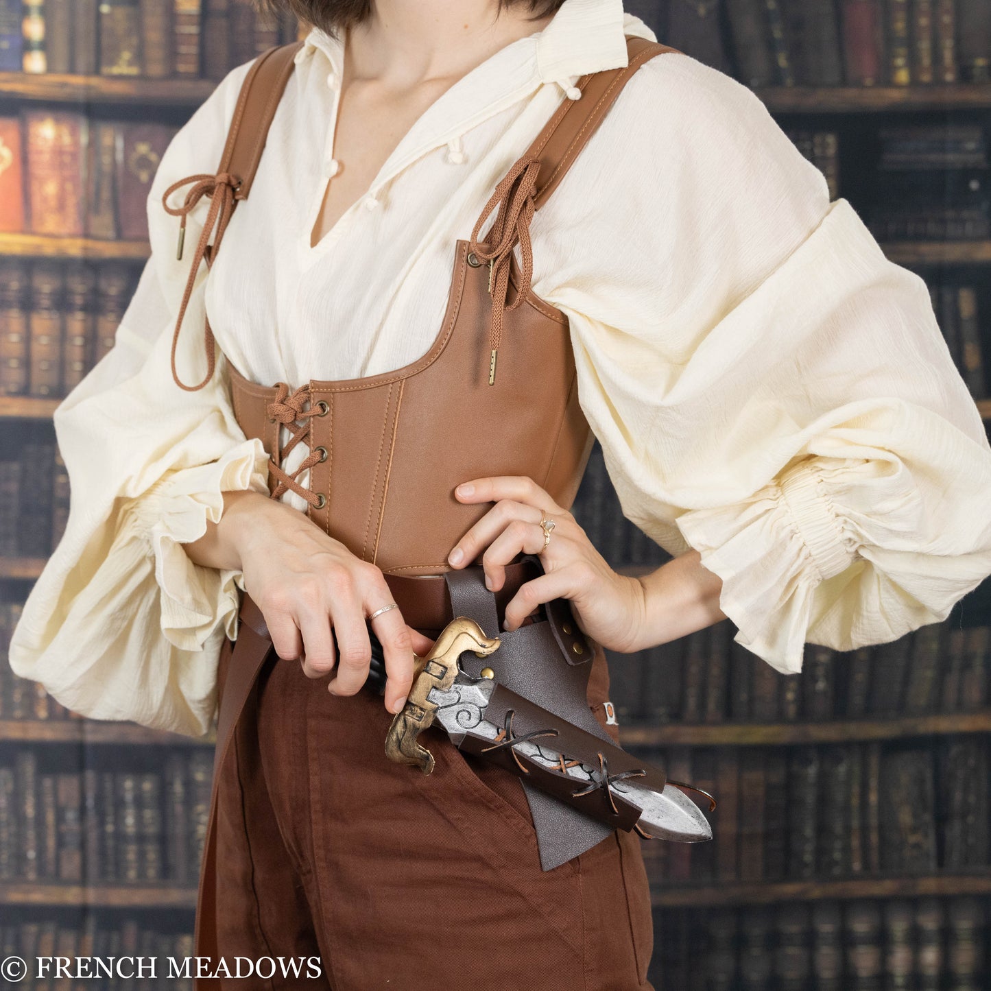 Brown leather sword scabbard with adjustable lacing shown on medieval costume with cream blouse in library setting