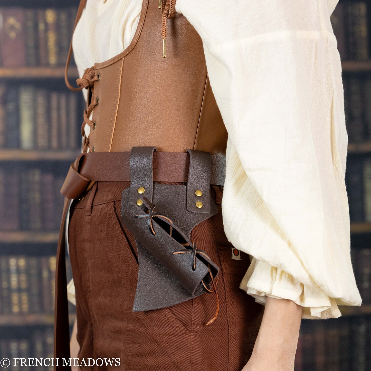 Brown leather sword scabbard with adjustable lacing worn on belt against medieval costume and library background