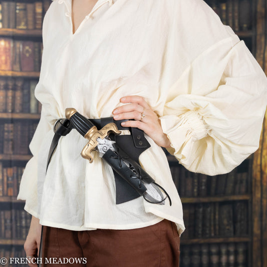 Black sword scabbard with adjustable lacing worn on belt against white renaissance blouse in library setting