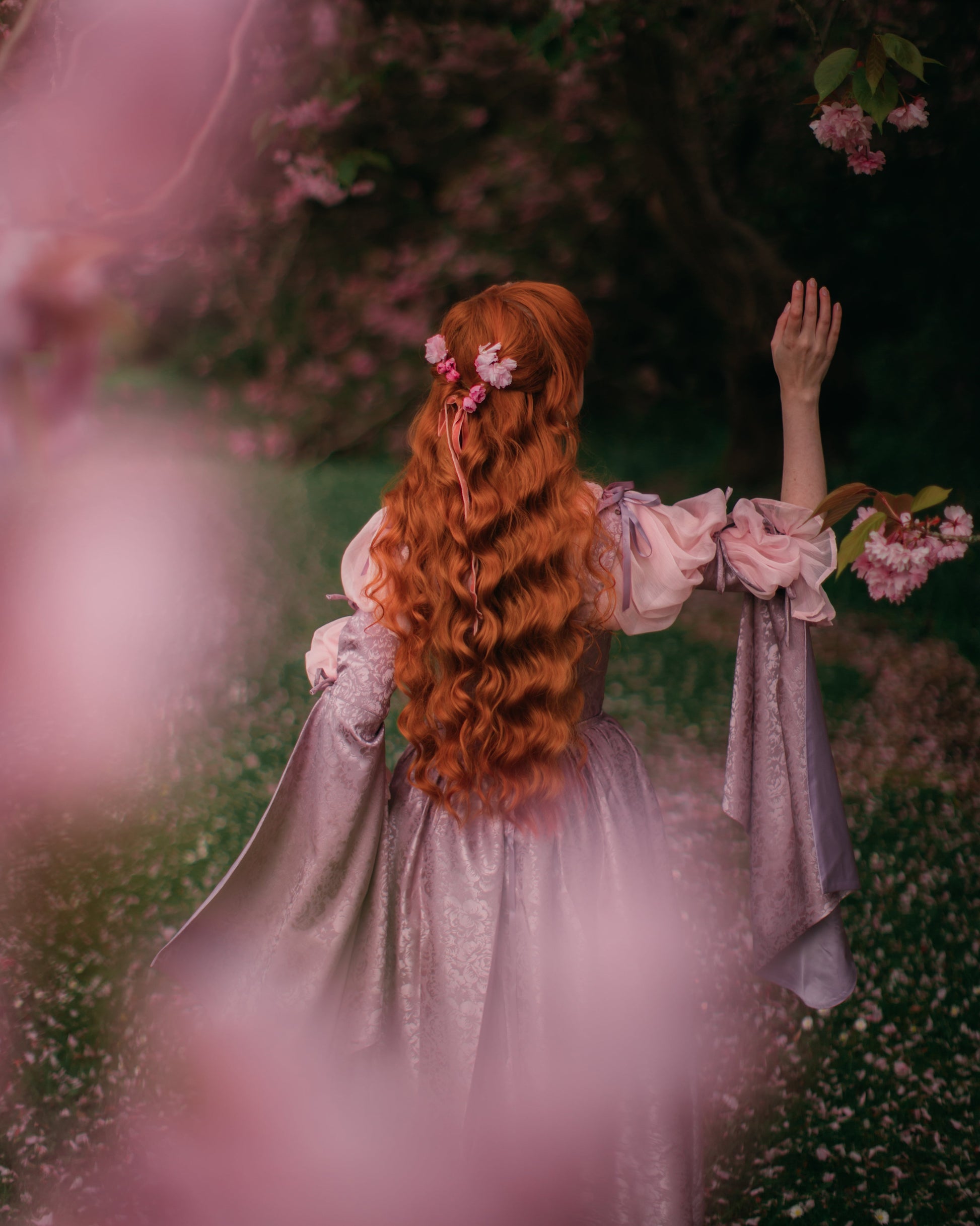 Lavender Floral Satin Corset Dress shown from back with long red hair in enchanted garden with blooming flowers.
