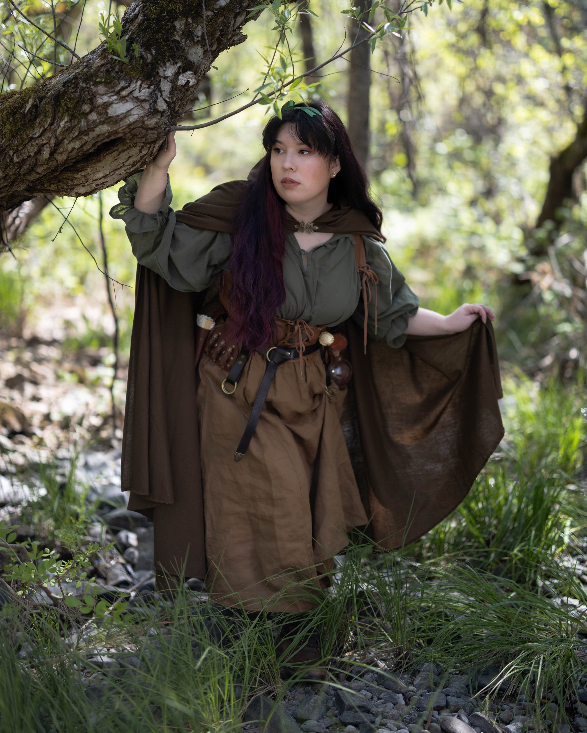 Woman wearing a Linen Renaissance Cloak in a forest setting during daylight, blending medieval and natural elements.